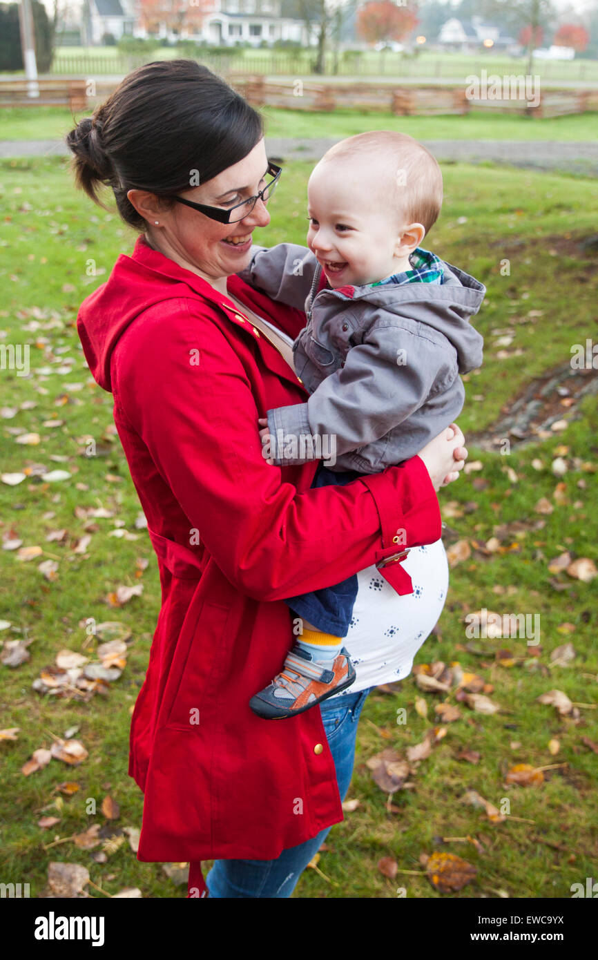 Eine schwangere Mutter hält ihr einjährigen Sohn beim Lachen. Stockfoto