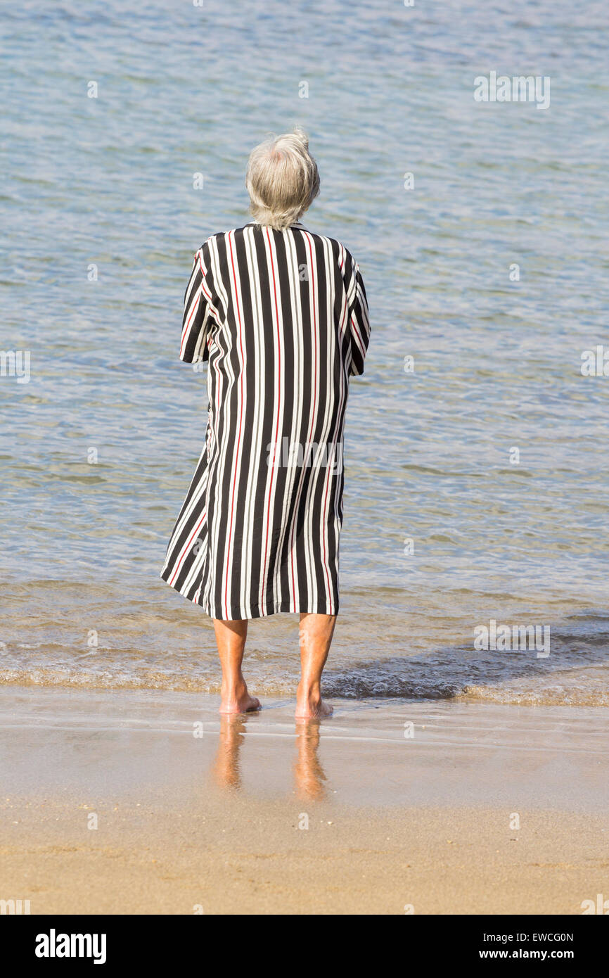 Ältere Frau zu Fuß entlang der Küste am Strand Stockfoto