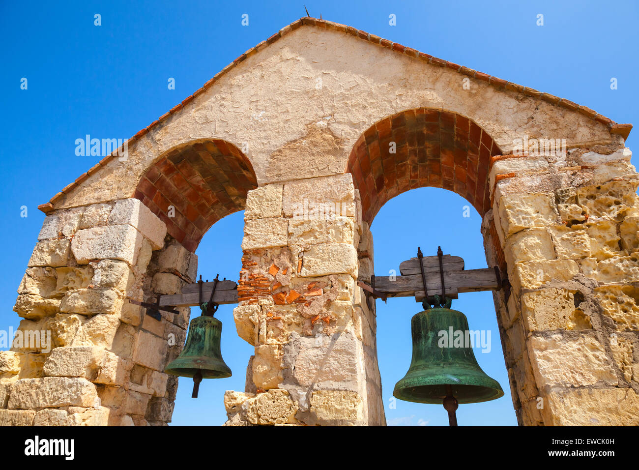 Mittelalterliche steinerne Burg in der Stadt von Calafell, Spanien. Zwei Glocken hängen in Bögen über blauer Himmelshintergrund Stockfoto