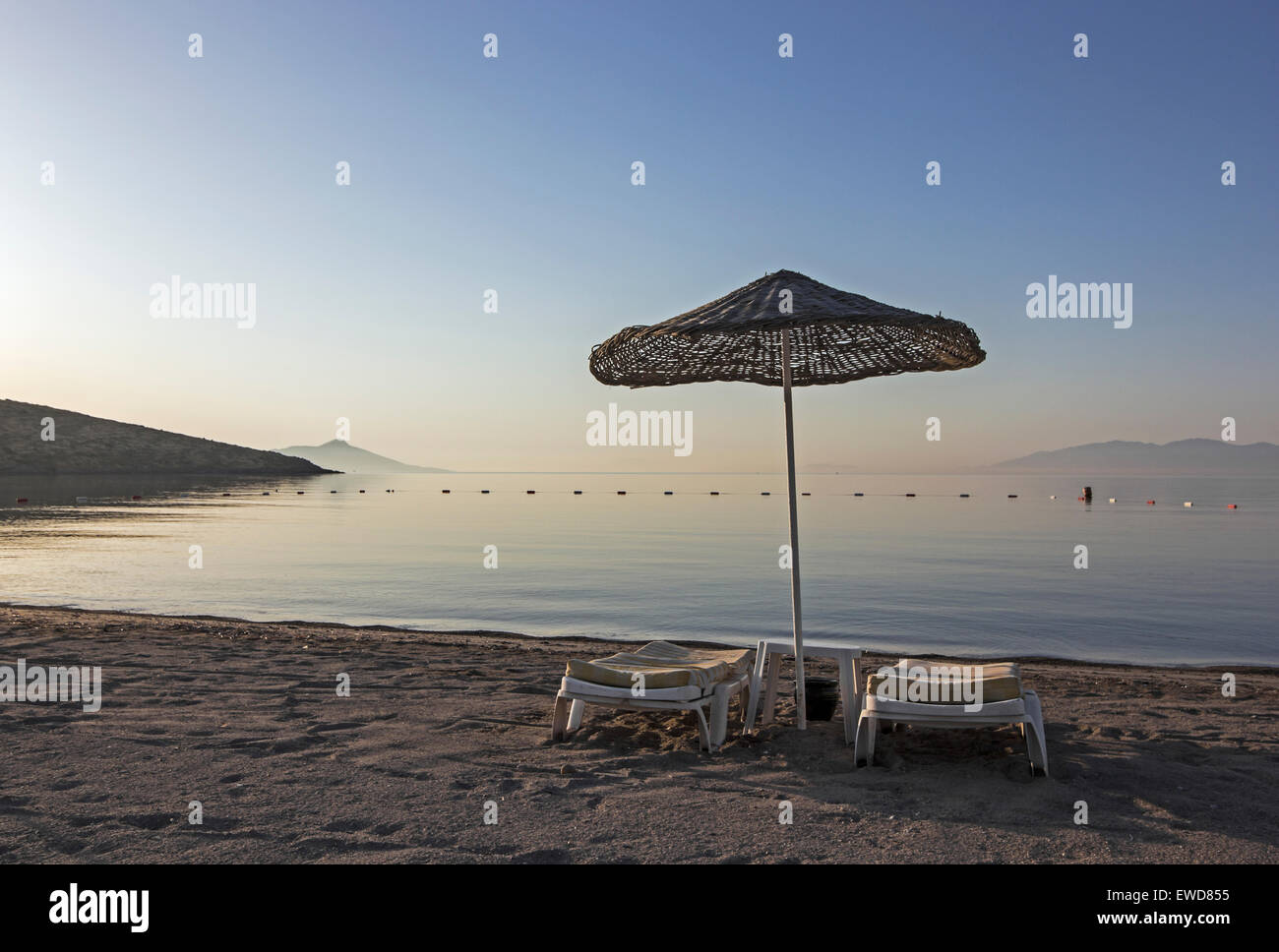 Strand, Regenschirm oder Sonnenschirm und Liegestühle am frühen Morgen an einem Akyarlar-Strand in der Türkei. Stockfoto