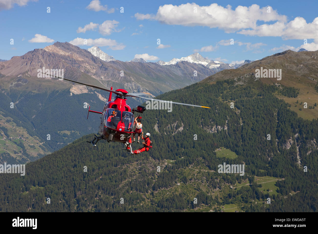 Ein Berg Rettung Notarzt ist unter einem Hubschrauber hoch über dem Boden hängen. Ein verletzter Wanderer ist auf Winde sein. Stockfoto
