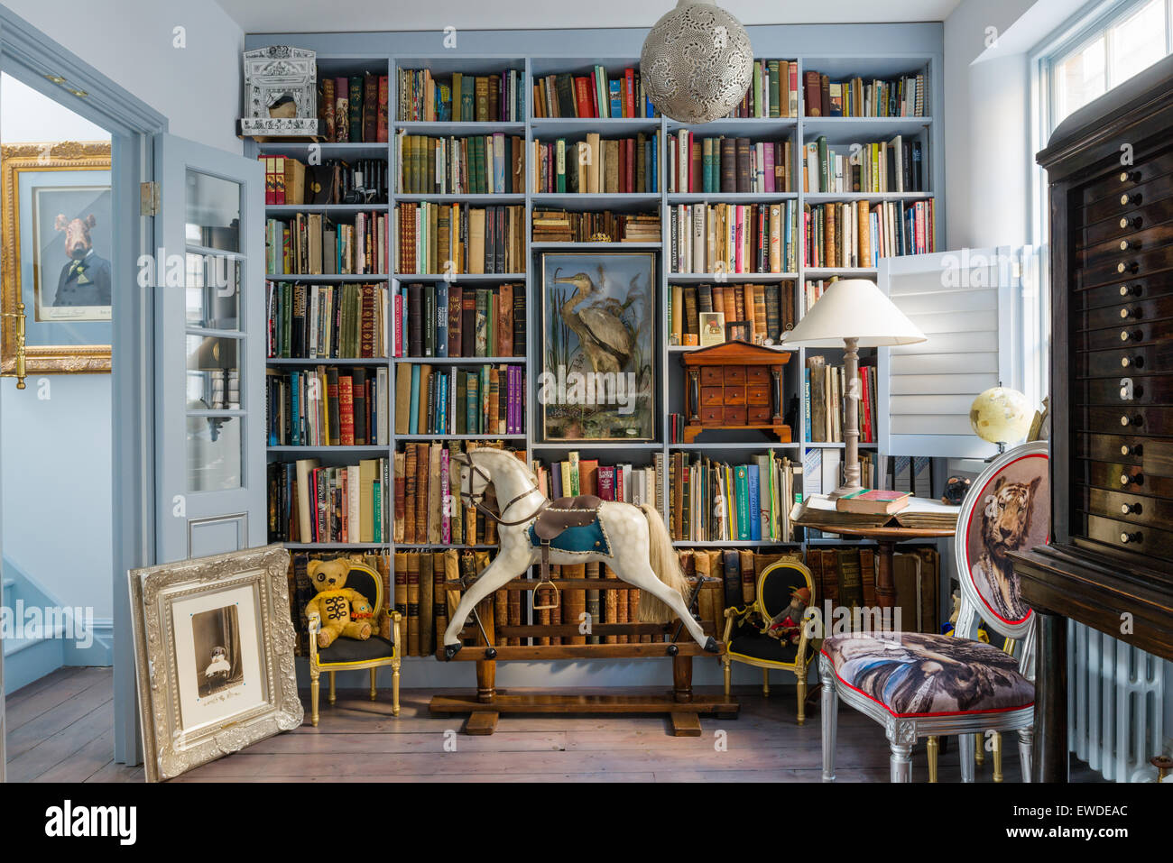 Blau lackierten Regalen in Bibliothek mit antiken Schaukelpferd und Cory Visitorian gepolsterten Stuhl Stockfoto