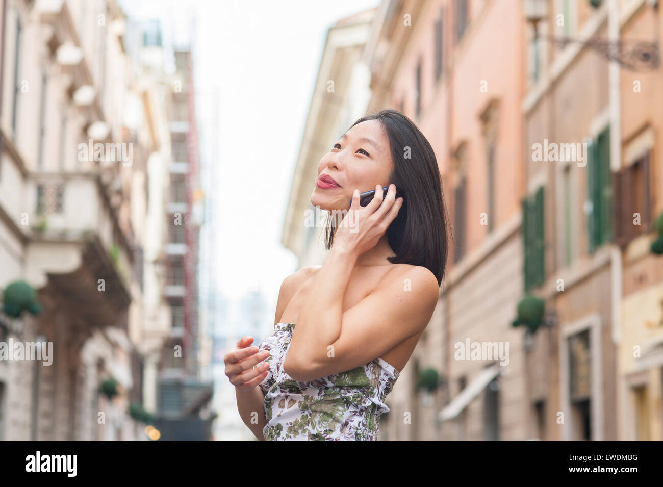 Junge schöne asiatische Frau Lächeln auf den Lippen und im Gespräch mit Handy urban outdoor Frühjahr dressing Stockfoto