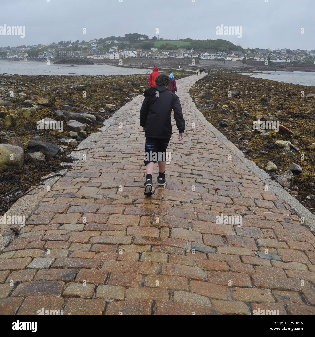 Familie zu Fuß in den Wind und Regen entlang St Michaels Mount Causeway, Rückkehr in die Stadt Marazion an einem nassen Sommertag Stockfoto