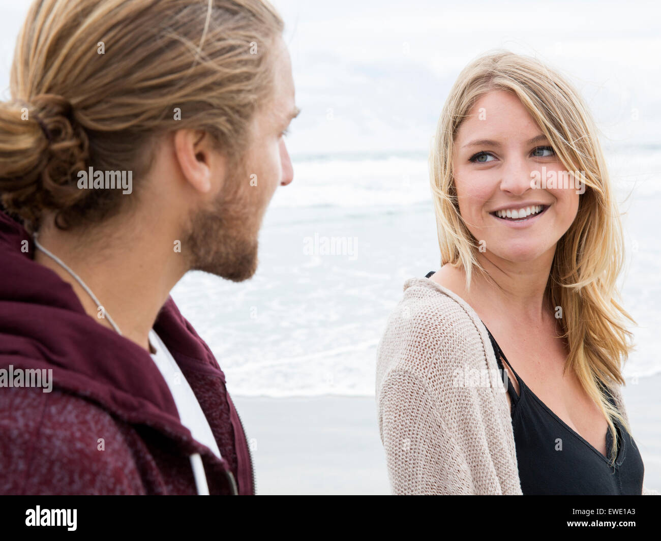Junger Mann und junge Frau am Strand, mit Blick auf einander, lächelnd Stockfoto