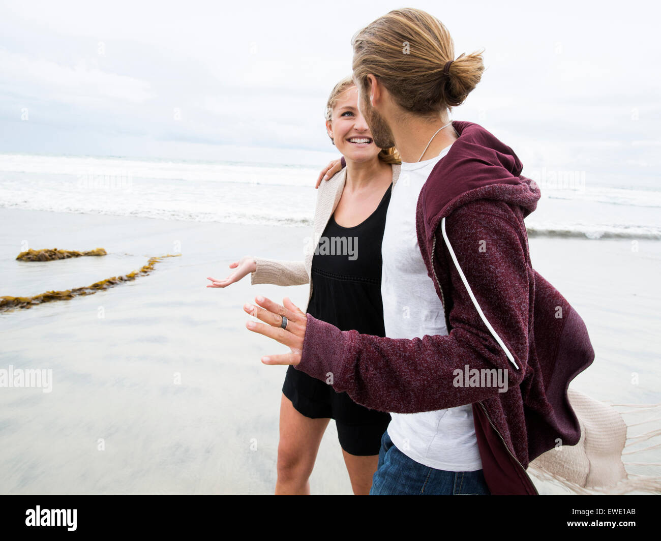 Junger Mann und junge Frau, die zu Fuß am Strand, Lächeln Stockfoto