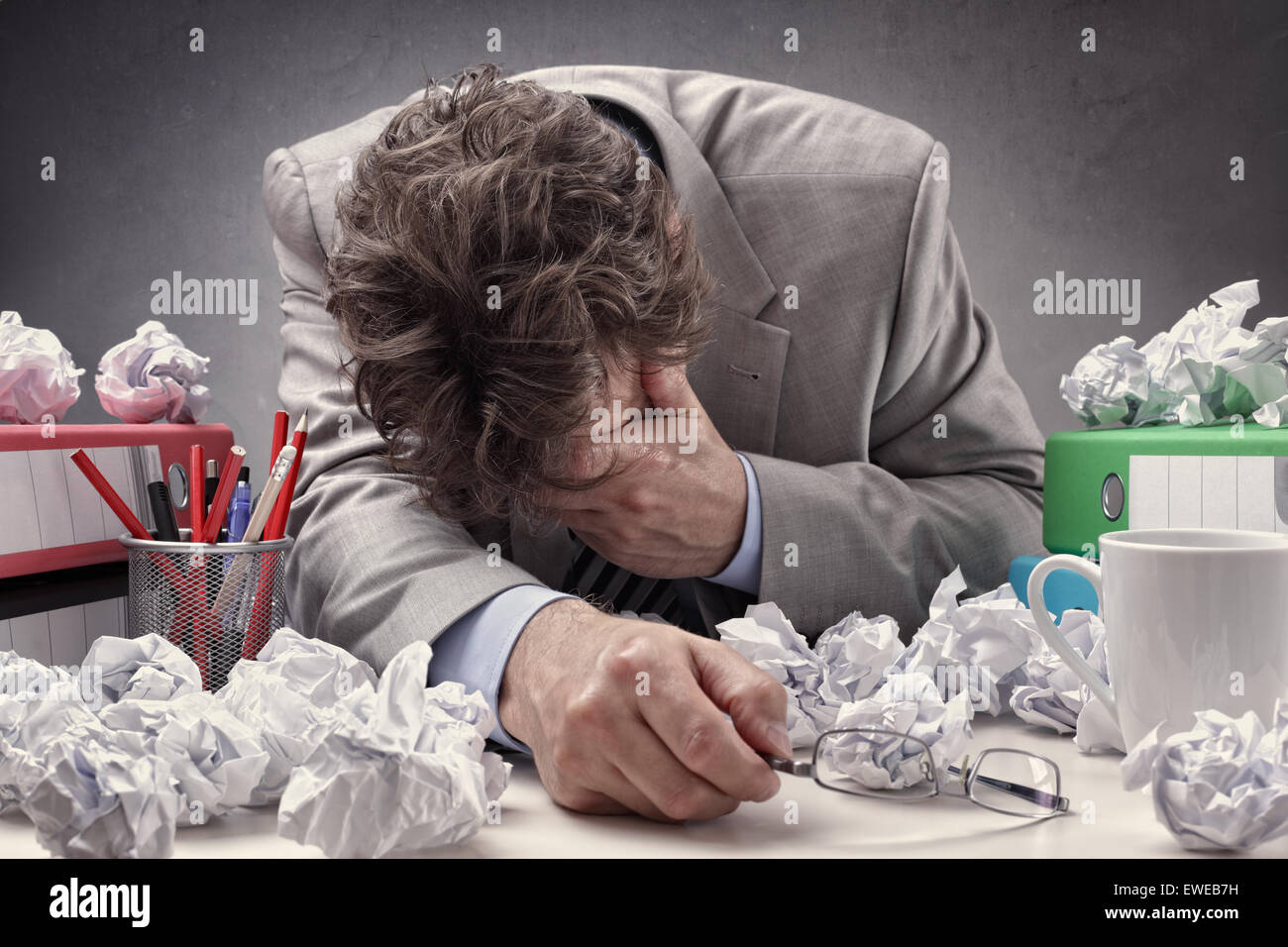 Überlastet, erschöpft und depressiv Geschäftsmann an seinem Schreibtisch mit einem Haufen von Arbeit oder Konzept für Frust, Stress und Autoren b Stockfoto