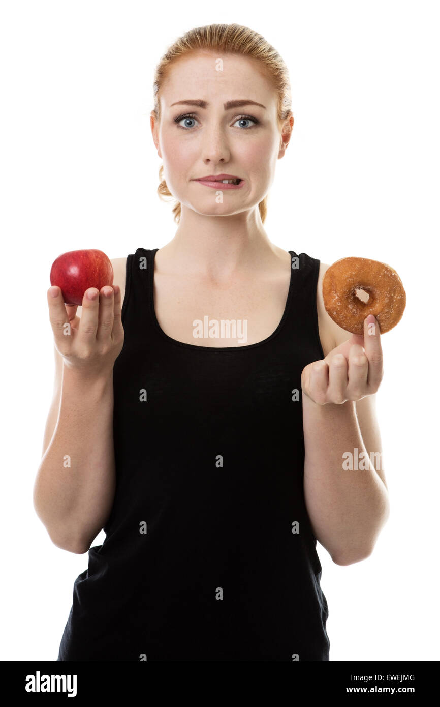 Frau trägt Sportkleidung hält einen Apfel und einen Donut nicht sicher, was zu essen Stockfoto