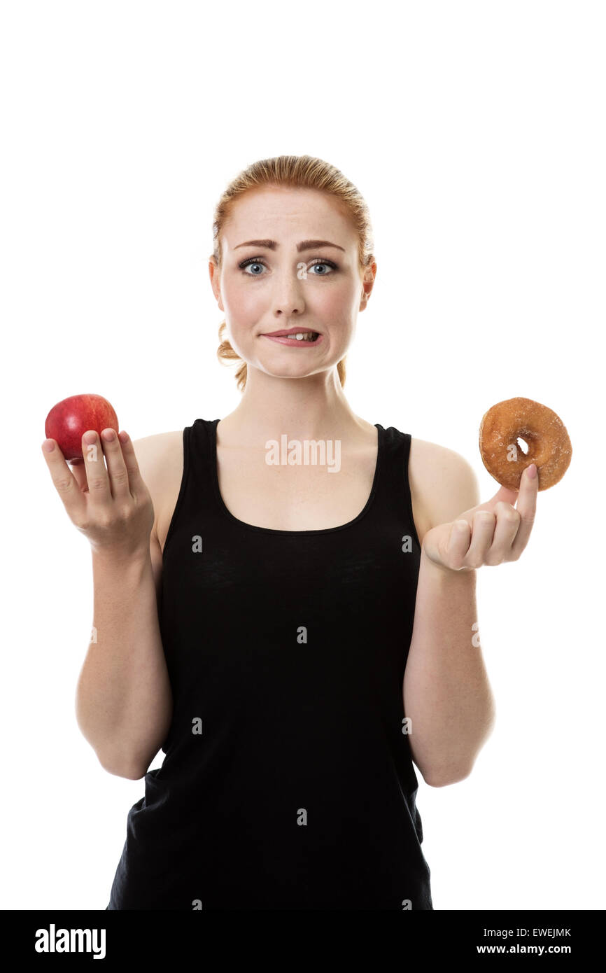 Frau trägt Sportkleidung hält einen Apfel und einen Donut nicht sicher, was zu essen Stockfoto