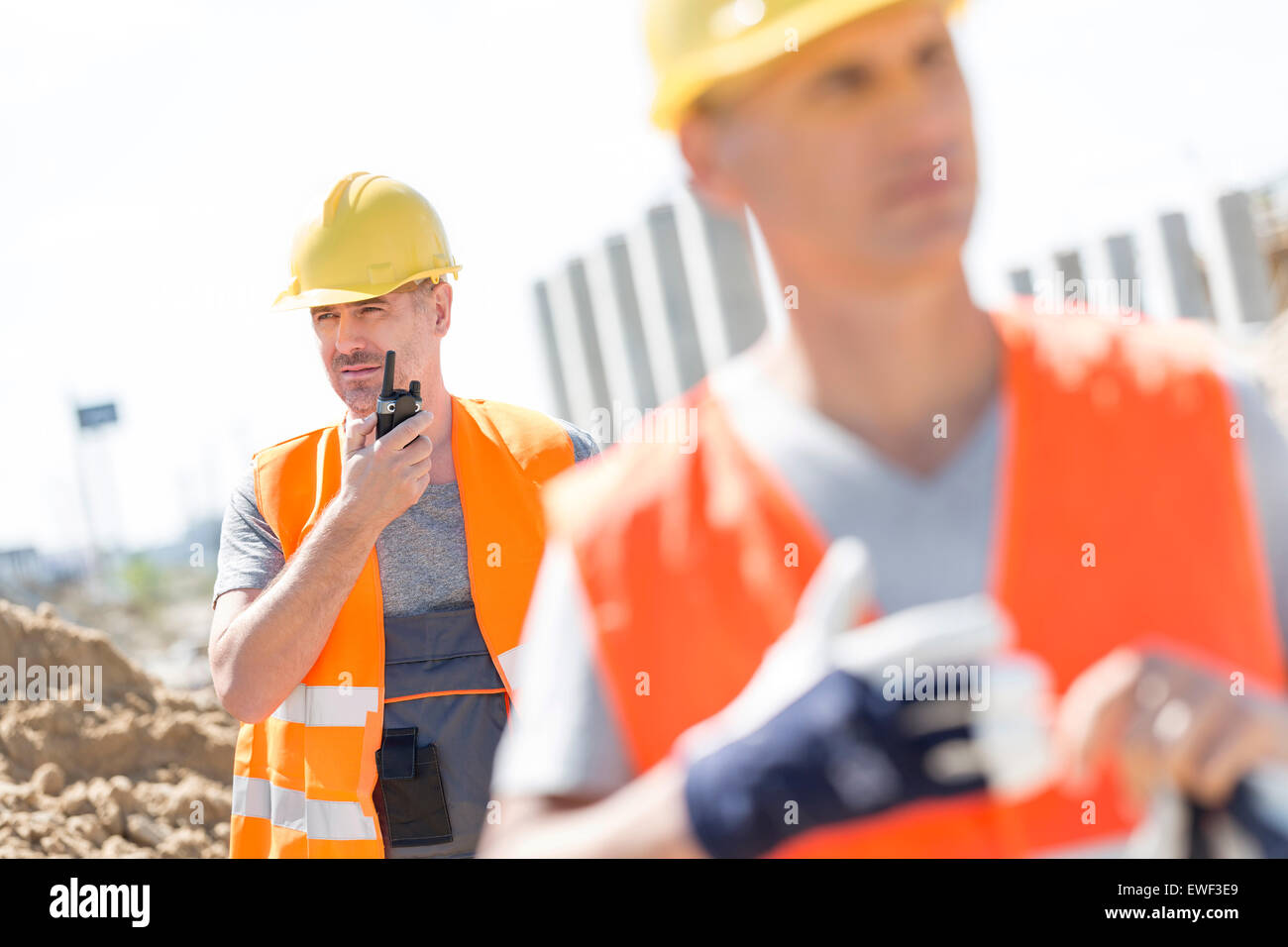 Im mittleren Alter männlicher Arbeitnehmer mit Walkie-talkie mit Kollegen im Vordergrund auf Baustelle Stockfoto