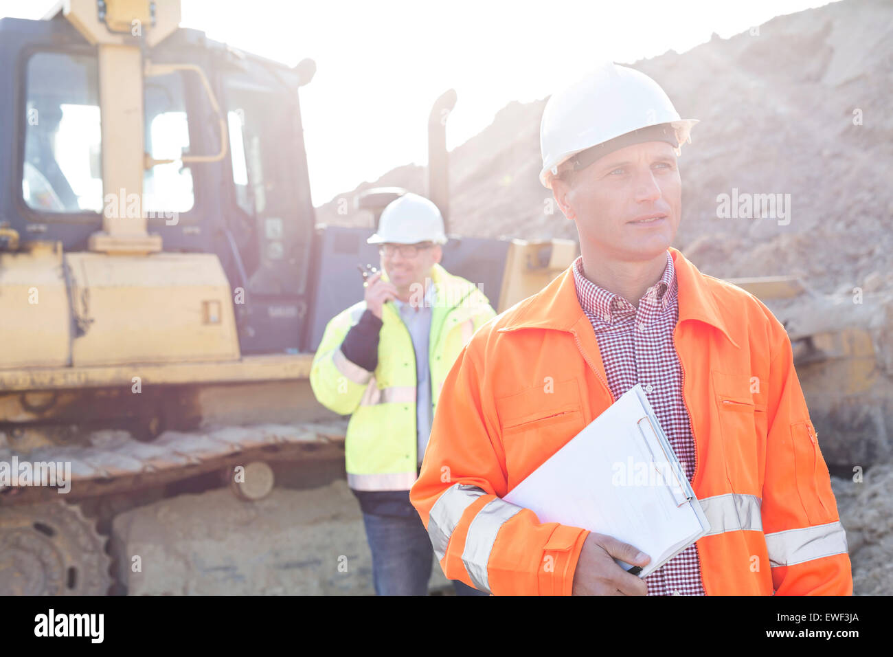 Ingenieur mit Zwischenablage auf Baustelle mit Kollegen im Hintergrund Stockfoto