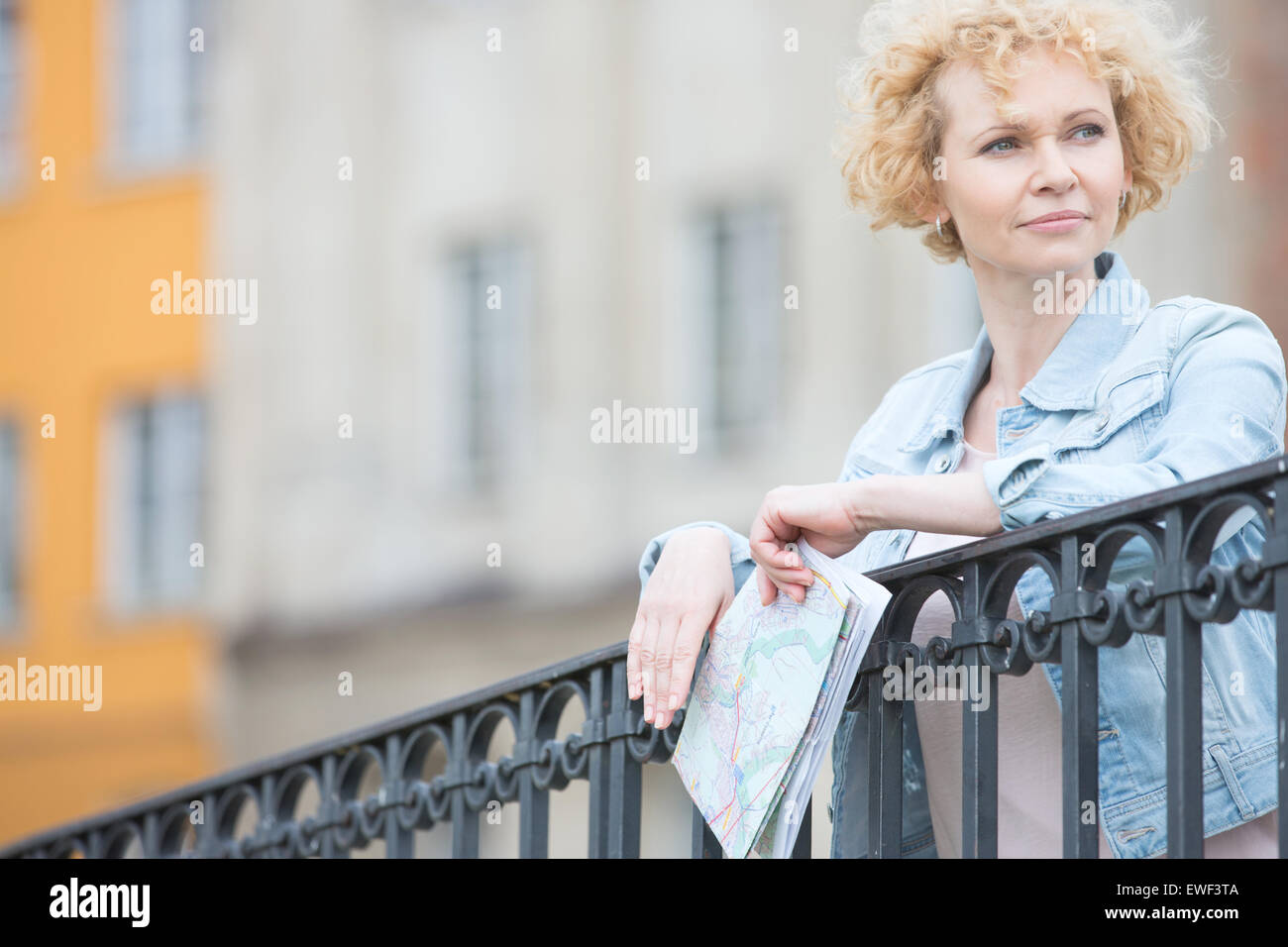 Nachdenkliche Frau mittleren Alters halten Karte und stützte sich auf Geländer Stockfoto