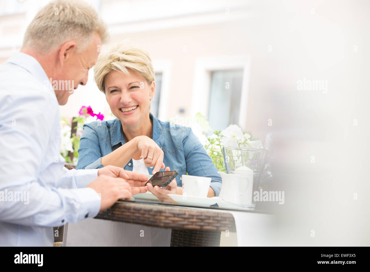 Glückliches Paar mittleren Alters mit Handy im Straßencafé Stockfoto