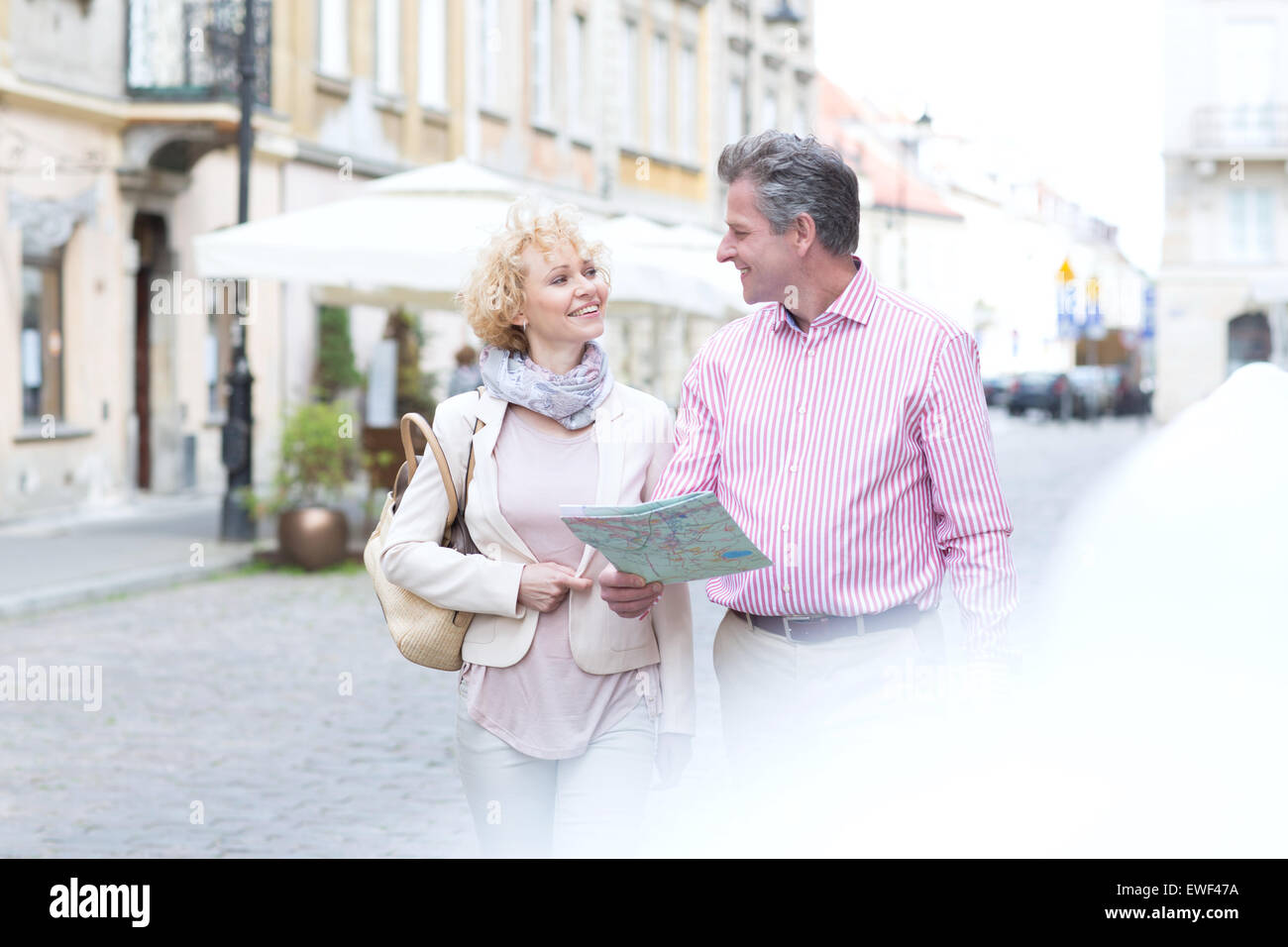 Lächelnde Paar mittleren Alters mit Karte sahen einander während des Gehens in Stadt Stockfoto