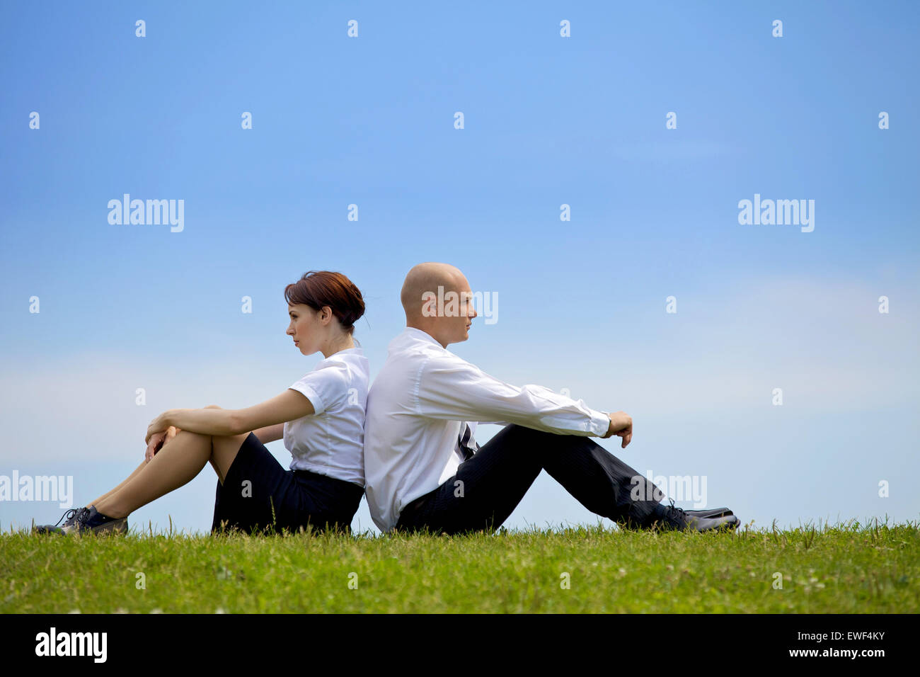 Geschäft paar sitzen Rücken an Rücken auf dem Rasen Stockfoto
