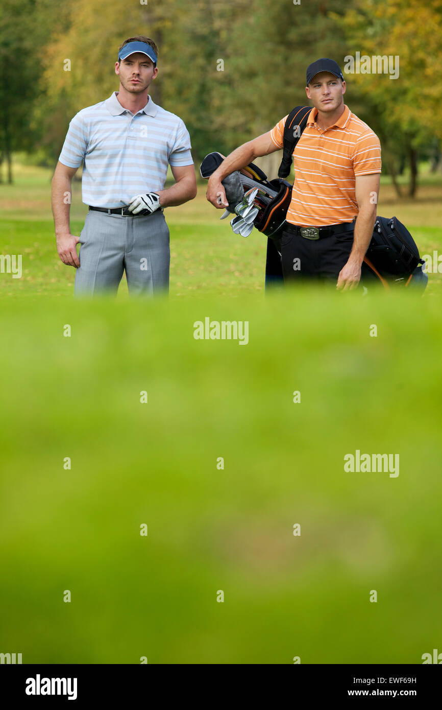Junge Männer stehen auf Golfplatz Tragetaschen Stockfoto