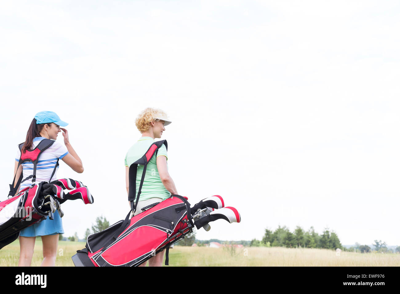 Rückansicht der Frauen mit Golfclub Taschen am Kurs gegen den klaren Himmel Stockfoto