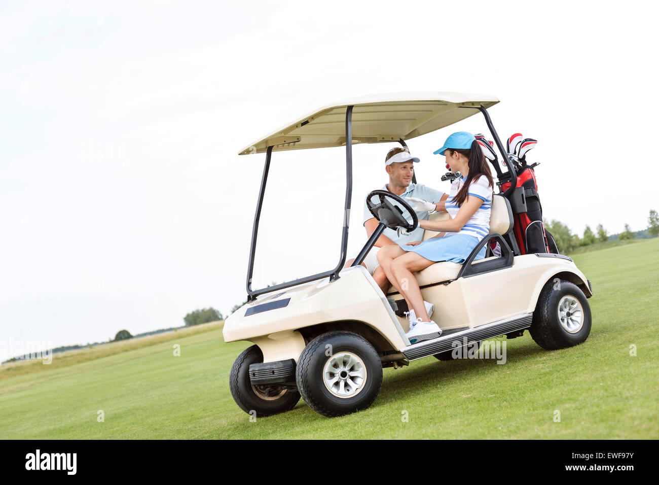 Paar sahen einander beim Sitzen im Golf-Cart gegen klaren Himmel Stockfoto