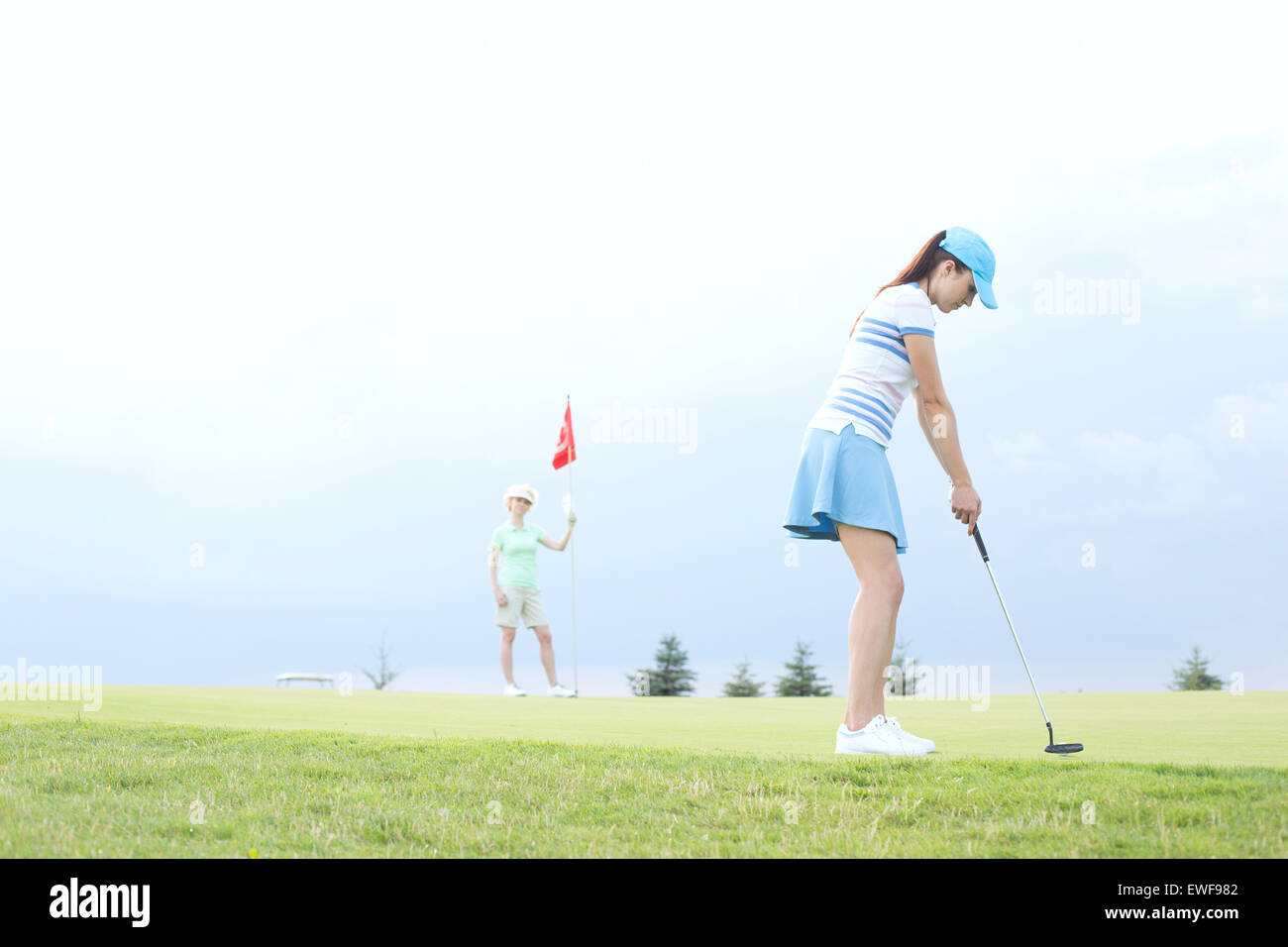 Frau spielt Golf mit Freundin gegen Himmel Stockfoto