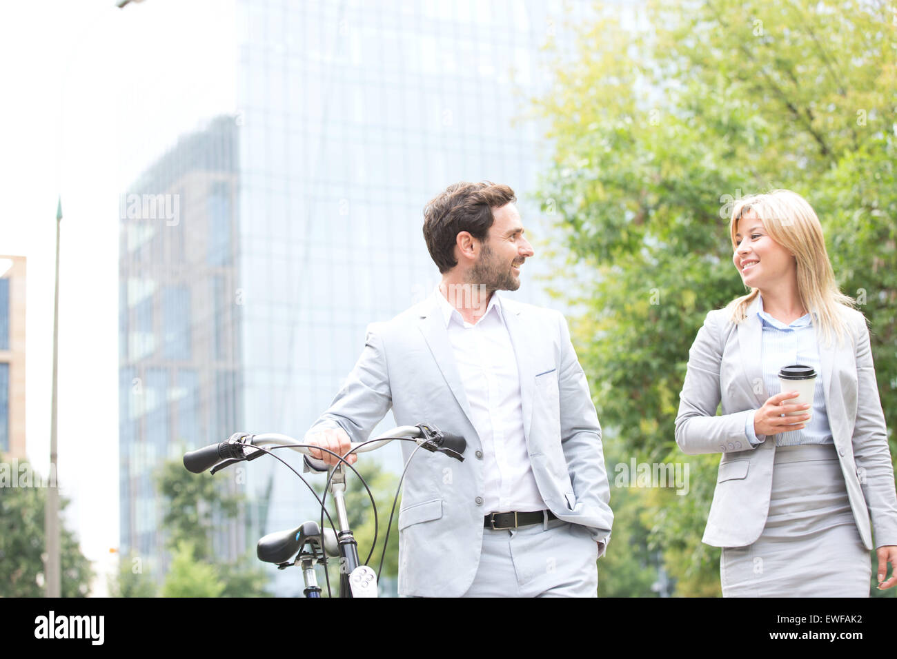 Geschäftsleute mit Fahrrad und Einweg-Cup im Gespräch während des Gehens im freien Stockfoto