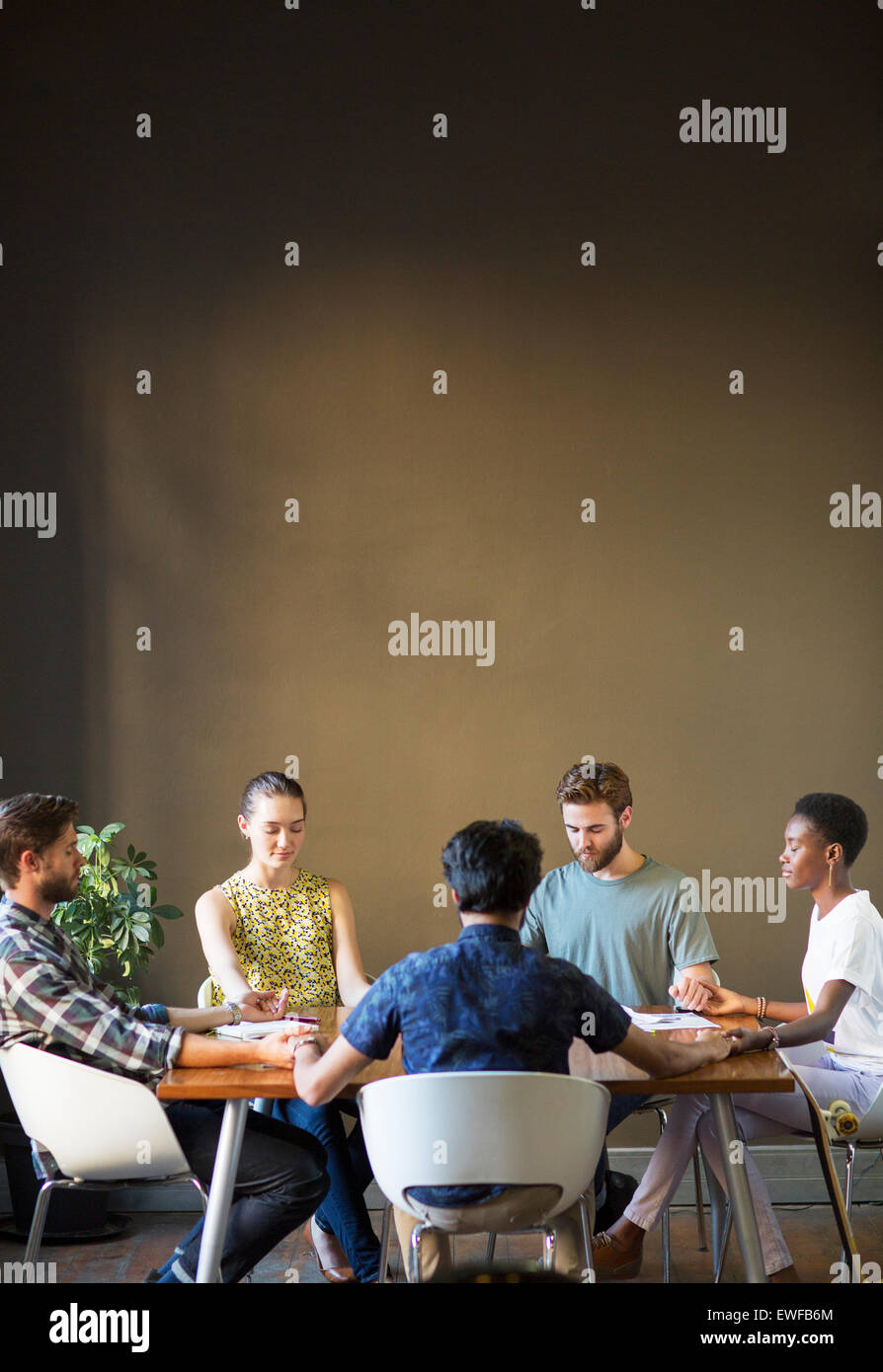 Heitere casual Business-Leute, die Hand in Hand mit Augen geschlossen am Bürotisch Stockfoto