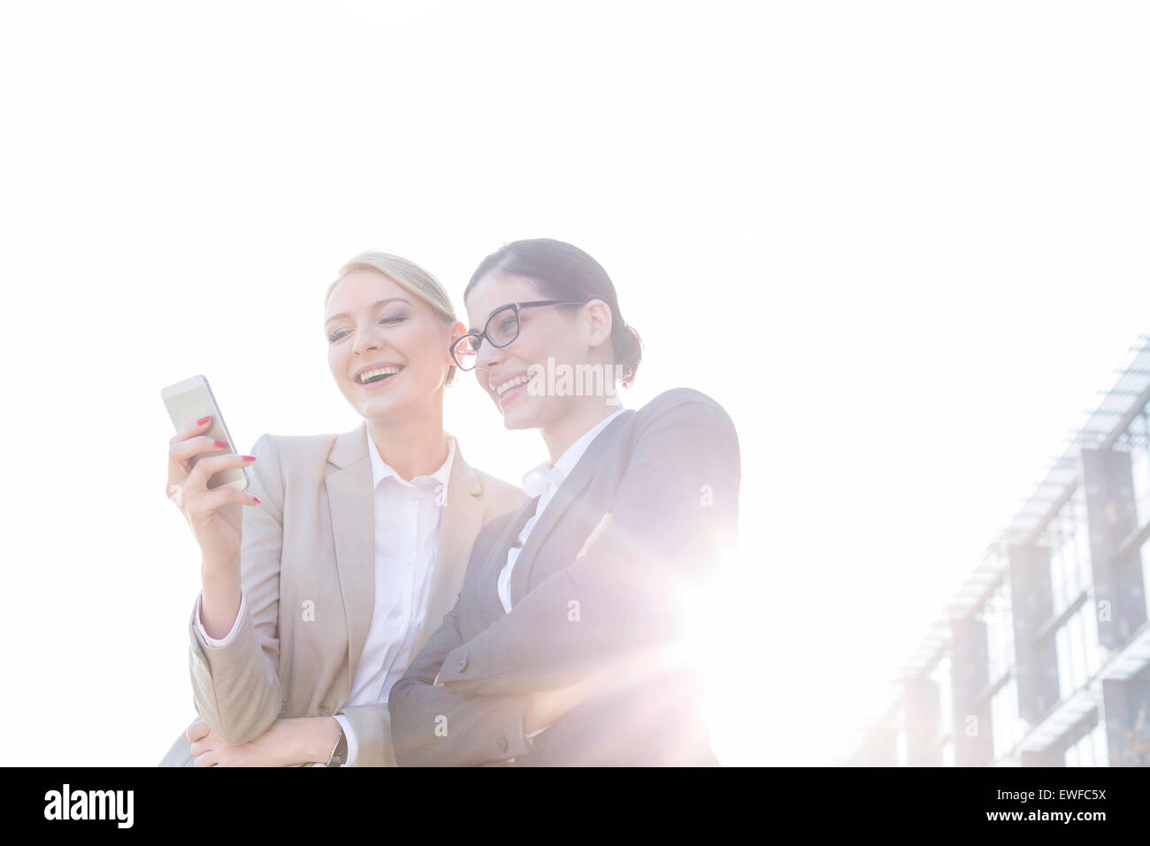 Niedrigen Winkel Ansicht glücklich Geschäftsfrauen mit Smartphone gegen klaren Himmel an sonnigen Tag Stockfoto