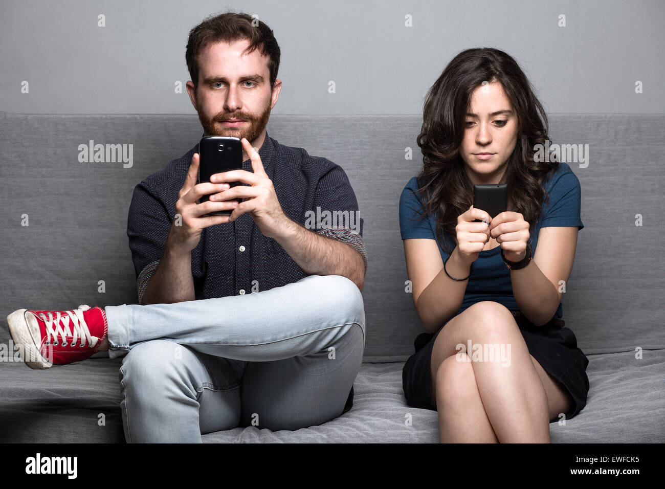 Junge Stille paar mit Smartphones, die auf einer Couch sitzend Stockfoto