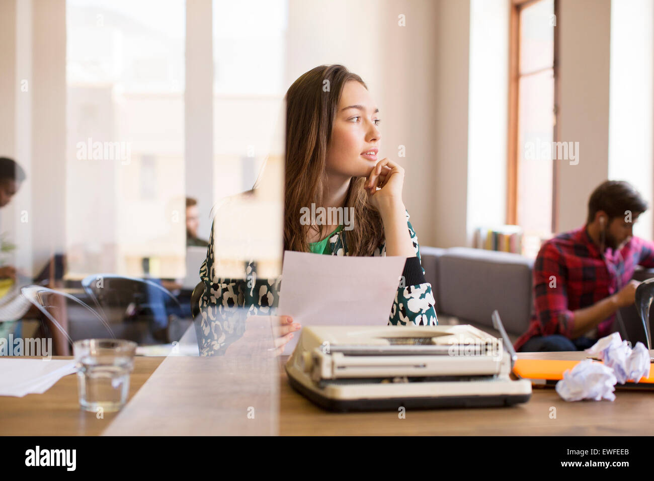 Nachdenklich kreative Geschäftsfrau mit Papierkram an Schreibmaschine im Büro Stockfoto