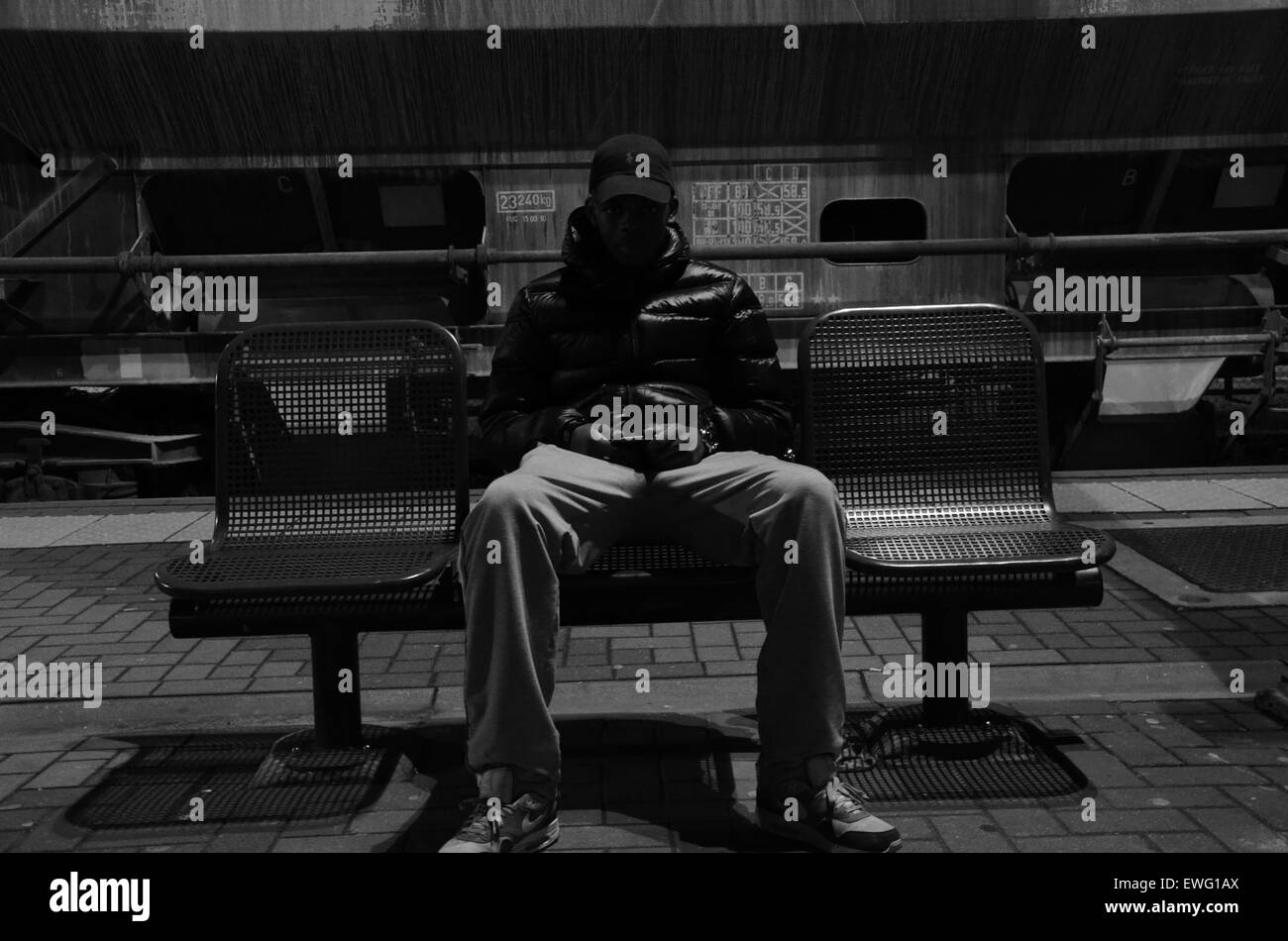 Ein Mann sitzt auf einer städtischen Bank, wahrscheinlich in einem öffentlichen Raum wie einem Park oder einem plaza. Das Bild fängt die ruhigen Momente des Stadtlebens und die Rolle der öffentlichen Sitzplätze in städtischen Umgebungen ein. Stockfoto
