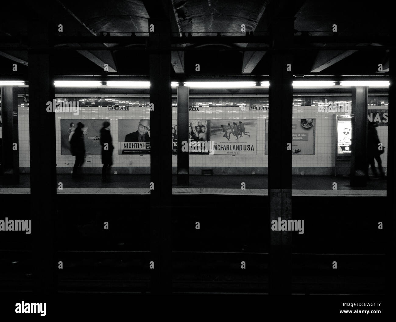 Dieses Schwarzweiß-Foto zeigt das Innere des U-Bahnhofs Nassau mit großen Säulen und einer Vintage-unterirdischen Werbung. Das Bild unterstreicht die historische Architektur und das Design des U-Bahn-Systems. Stockfoto