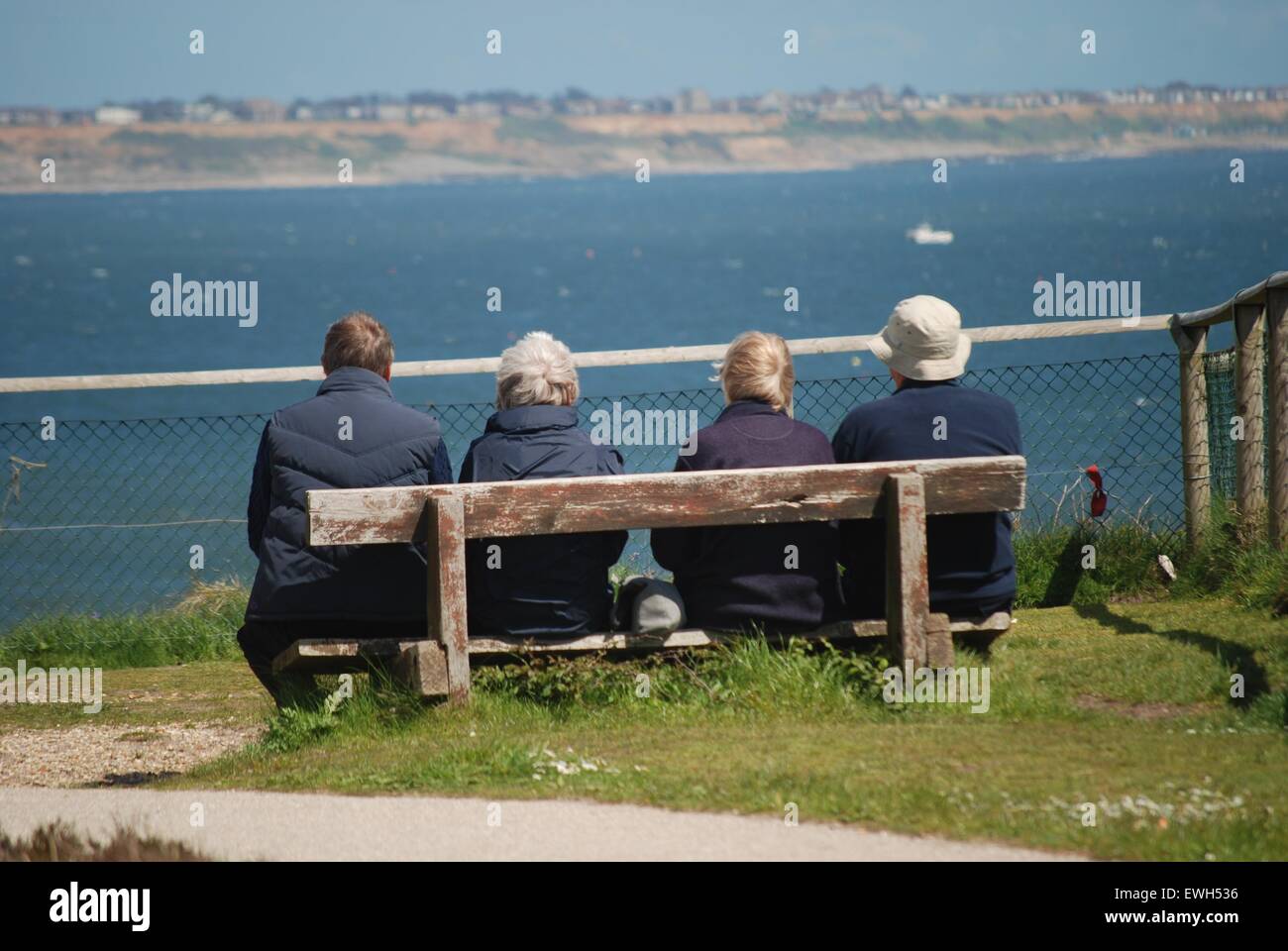 Vier ältere Freunde sitzen auf einer Bank mit Blick auf Meer Stockfoto