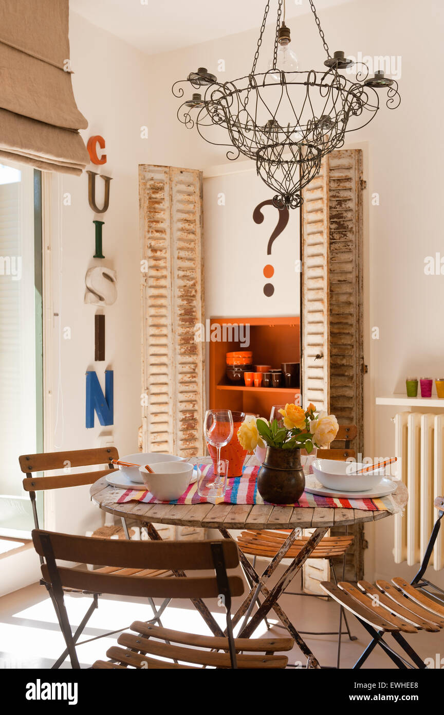 Französisch Draht Kronleuchter über dem Café-Tisch und Stühle in der Küche mit rustikalen Leinen Vorhang Stockfoto