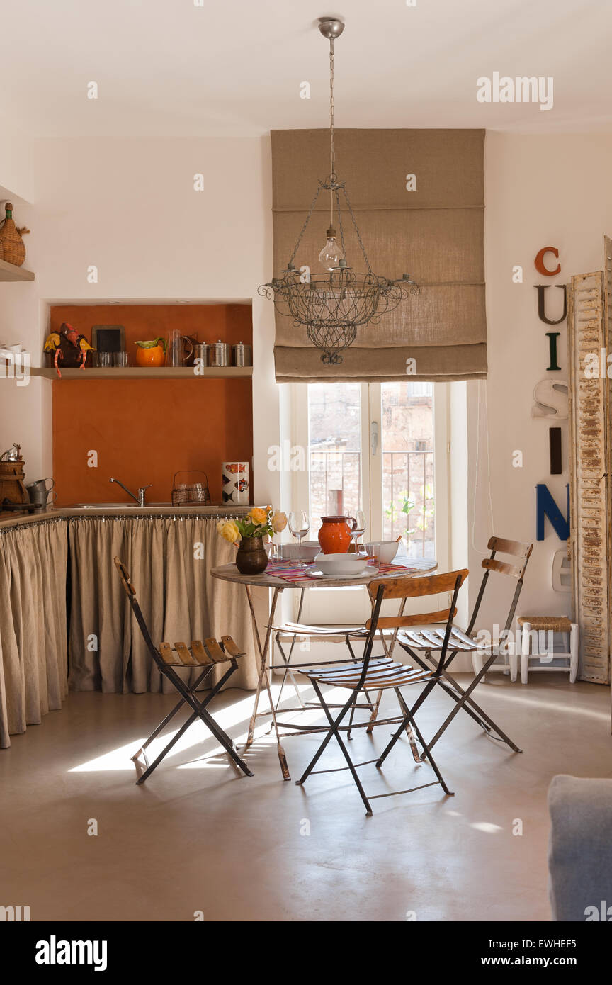 Französisch Draht Kronleuchter über dem Café-Tisch und Stühle in der Küche mit rustikalen Leinen Vorhang Stockfoto