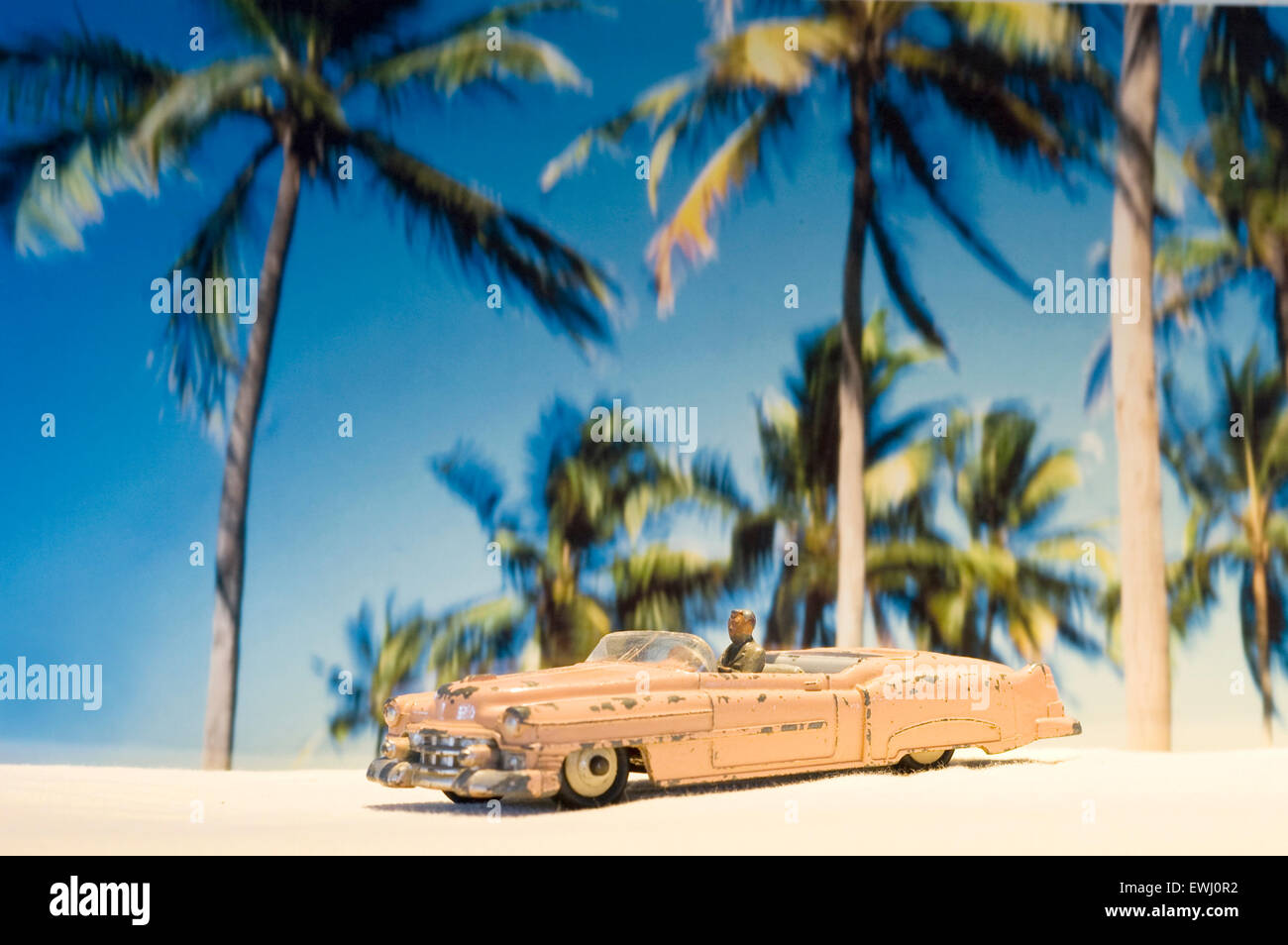 Ein abgenutztes und zerschmettertes pinkfarbenes Cadillac Dinky Auto Spielzeug in einer tropischen Umgebung mit Palmen am Strand Stockfoto