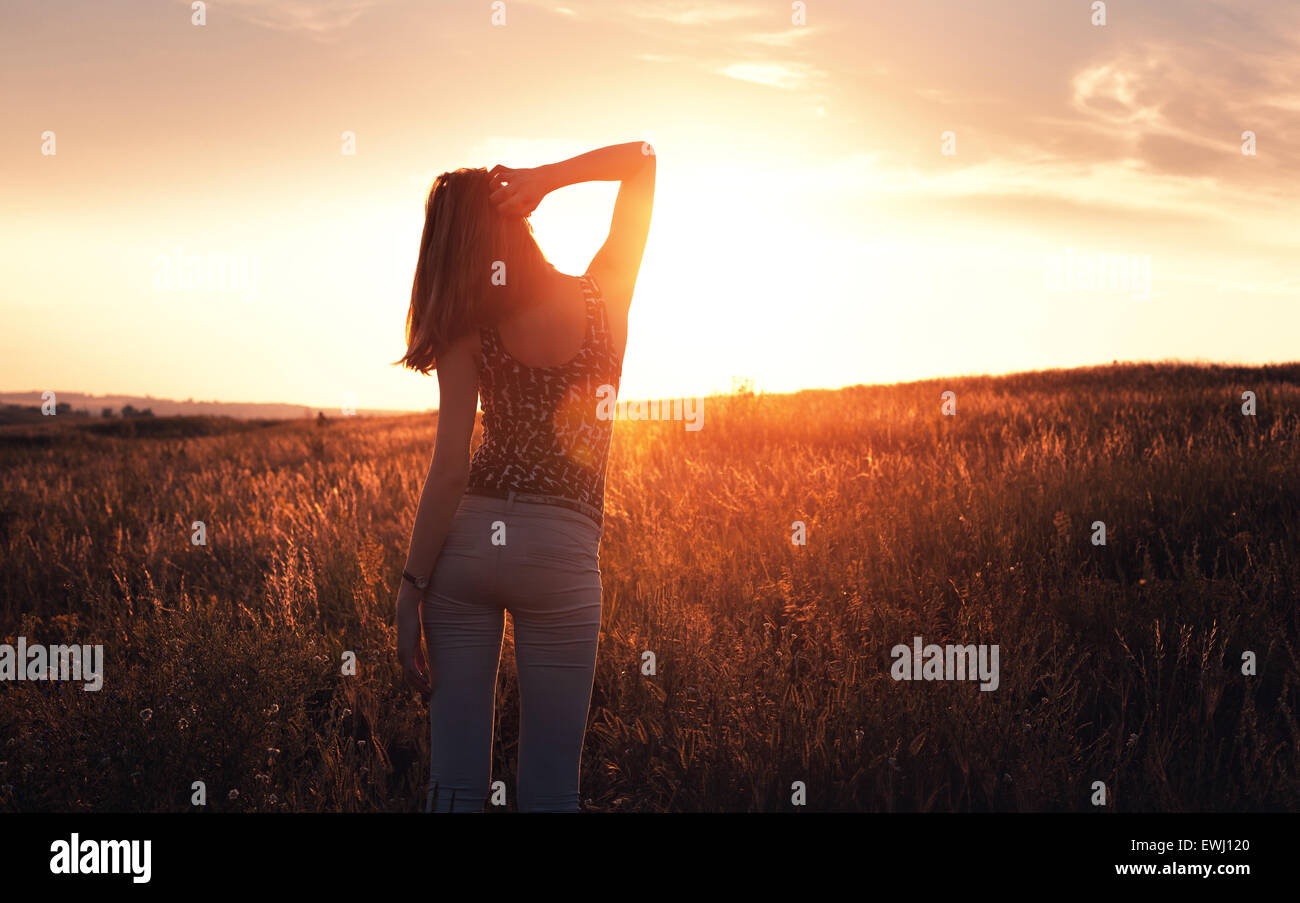 Frei glückliche junge Frau anheben Arme bei Sonnenuntergang im Feld im Sommer. Hintergrund Stockfoto