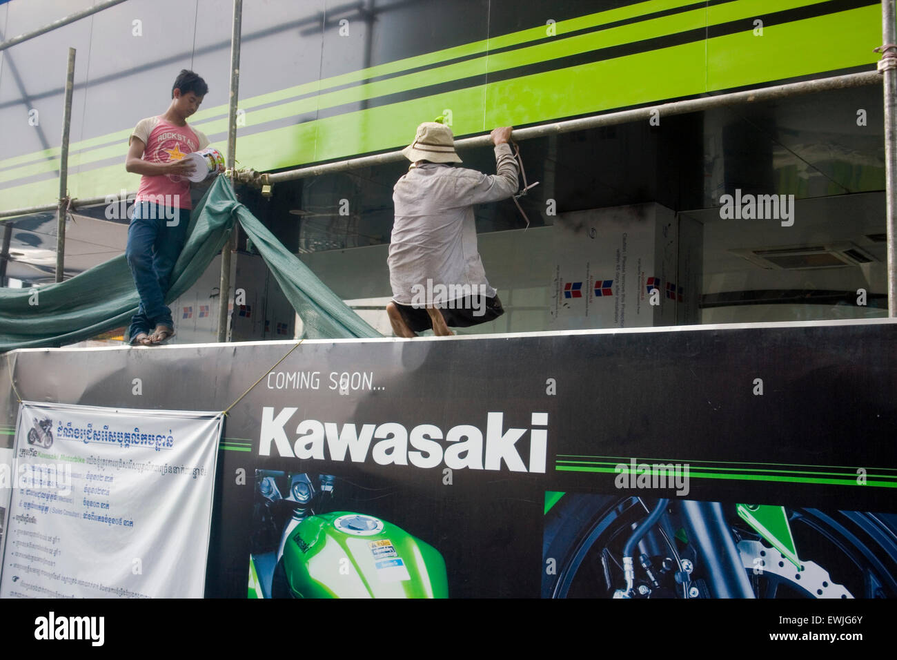 Zwei Männer malen einen neuen Kawasaki Motorrad Showroom über einer Stadt Straße in Phnom Penh, Kambodscha. Stockfoto
