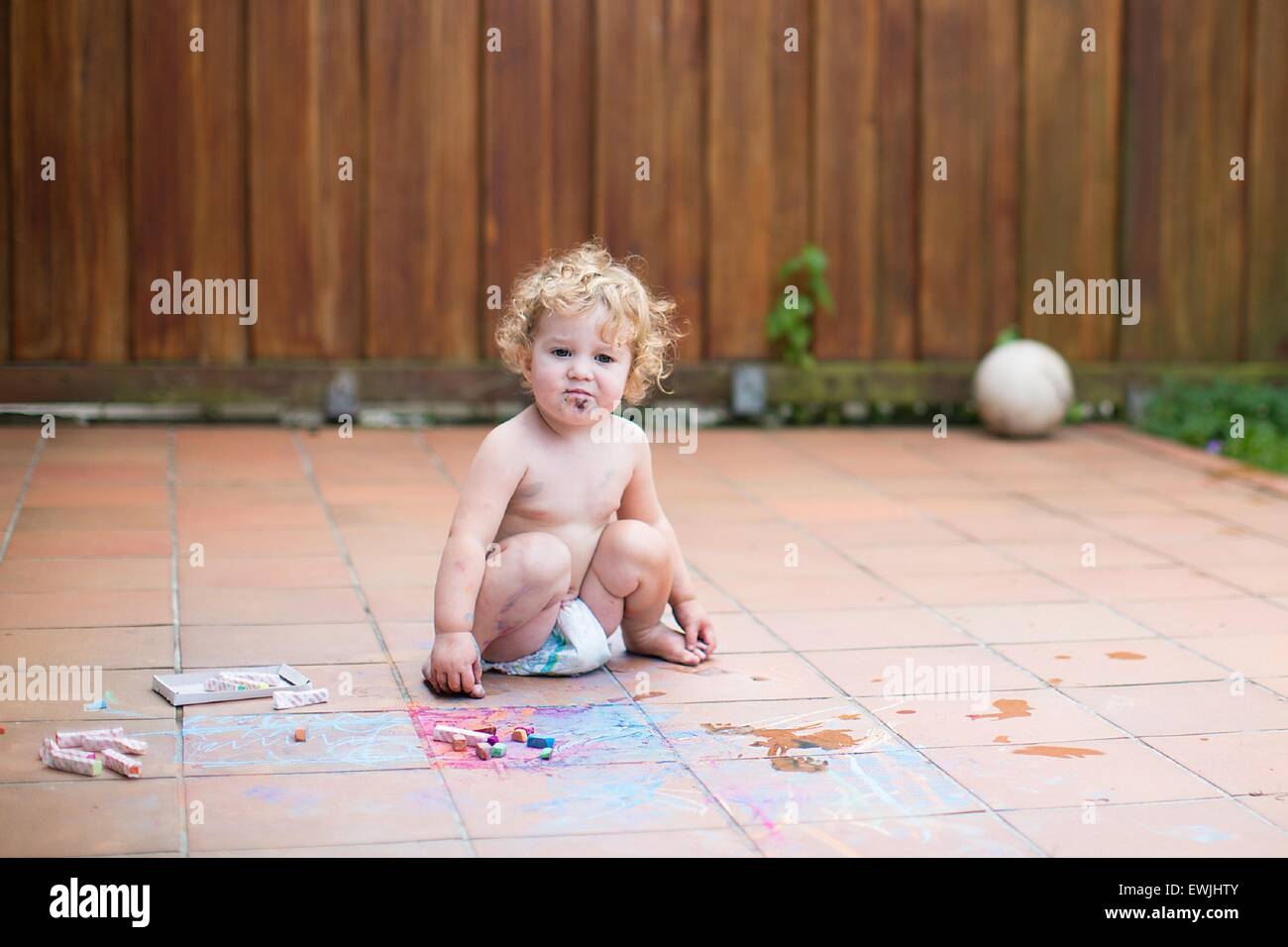 Lustiges kleines Mädchen tragen eine Windel Gemälde mit Kreide in den Hinterhof eines Hauses Stockfoto