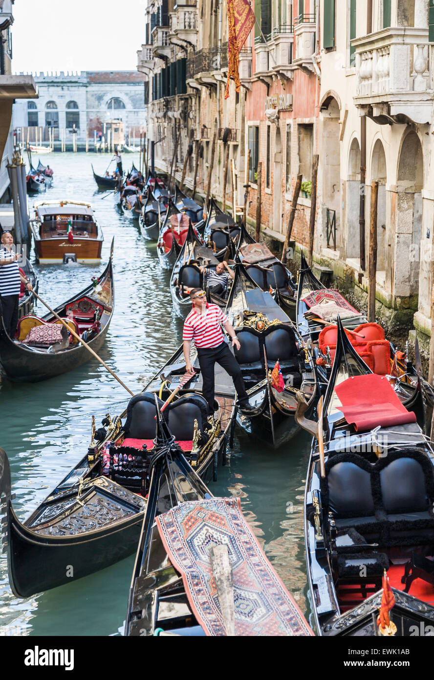 Gondeln vor Anker in einem Seitenkanal in Venedig, Gondoliere im traditionellen gestreiften Hemd wartet auf touristischen Kunden Stockfoto