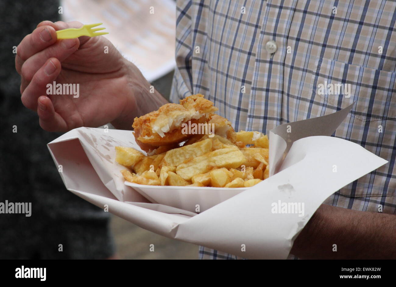 Ein Mann isst Fisch und Chips aus einem Fach im freien - Sommer, England UK Stockfoto