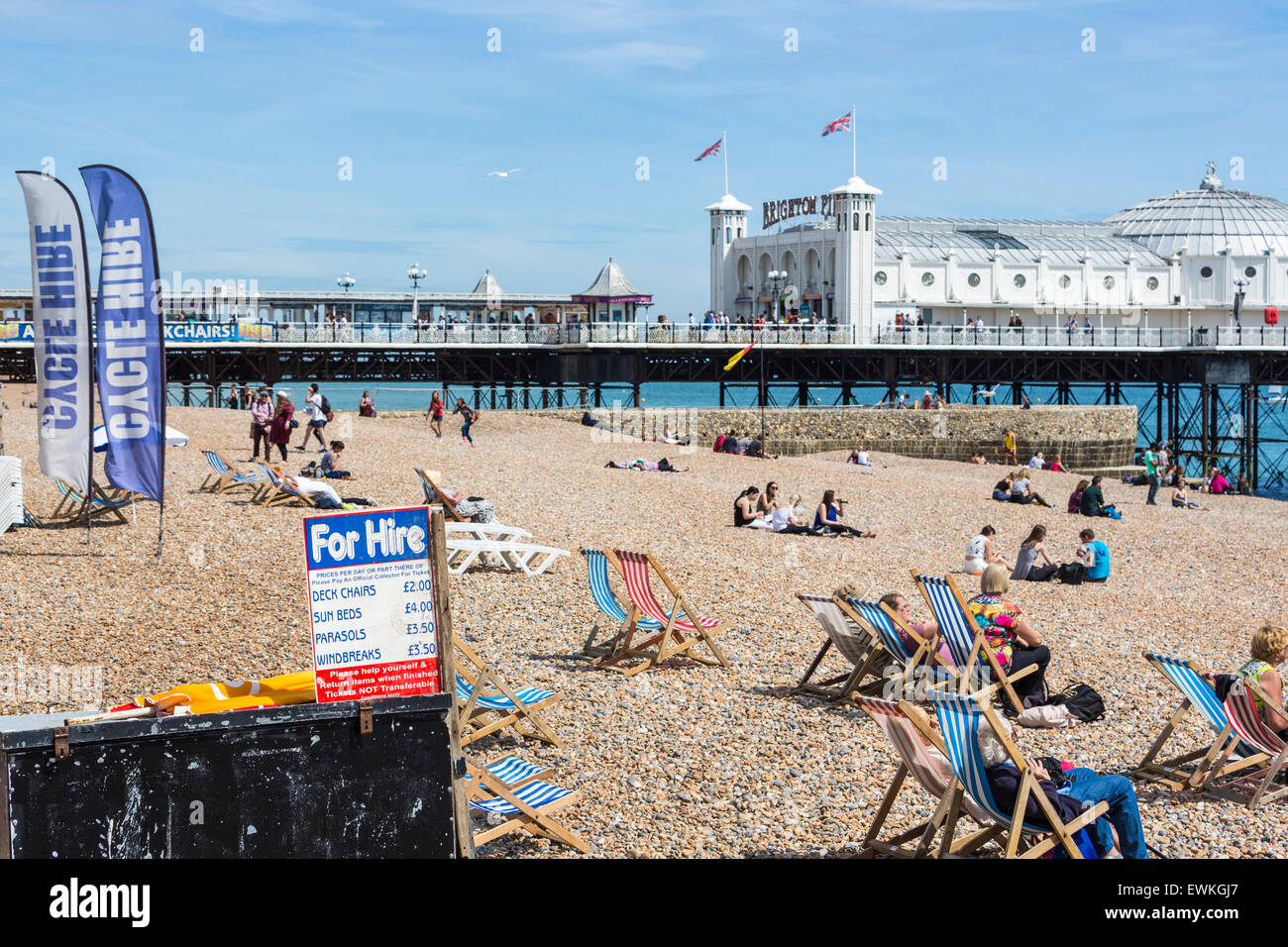 Urlauber entspannen Sie sich auf gemieteten gestreifte Liegestühle am Strand von Brighton an einem sonnigen Sommertag, Brighton, East Sussex, UK Stockfoto