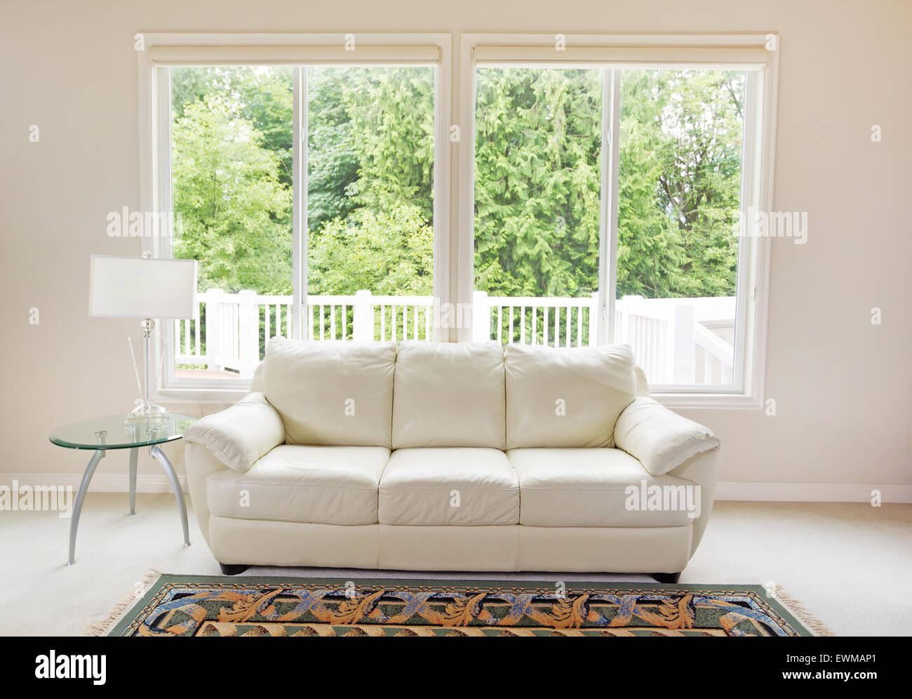 Saubere Familienzimmer mit weißen Ledercouch und große Fenster zeigen helle Grün der Bäume im Hintergrund. Stockfoto