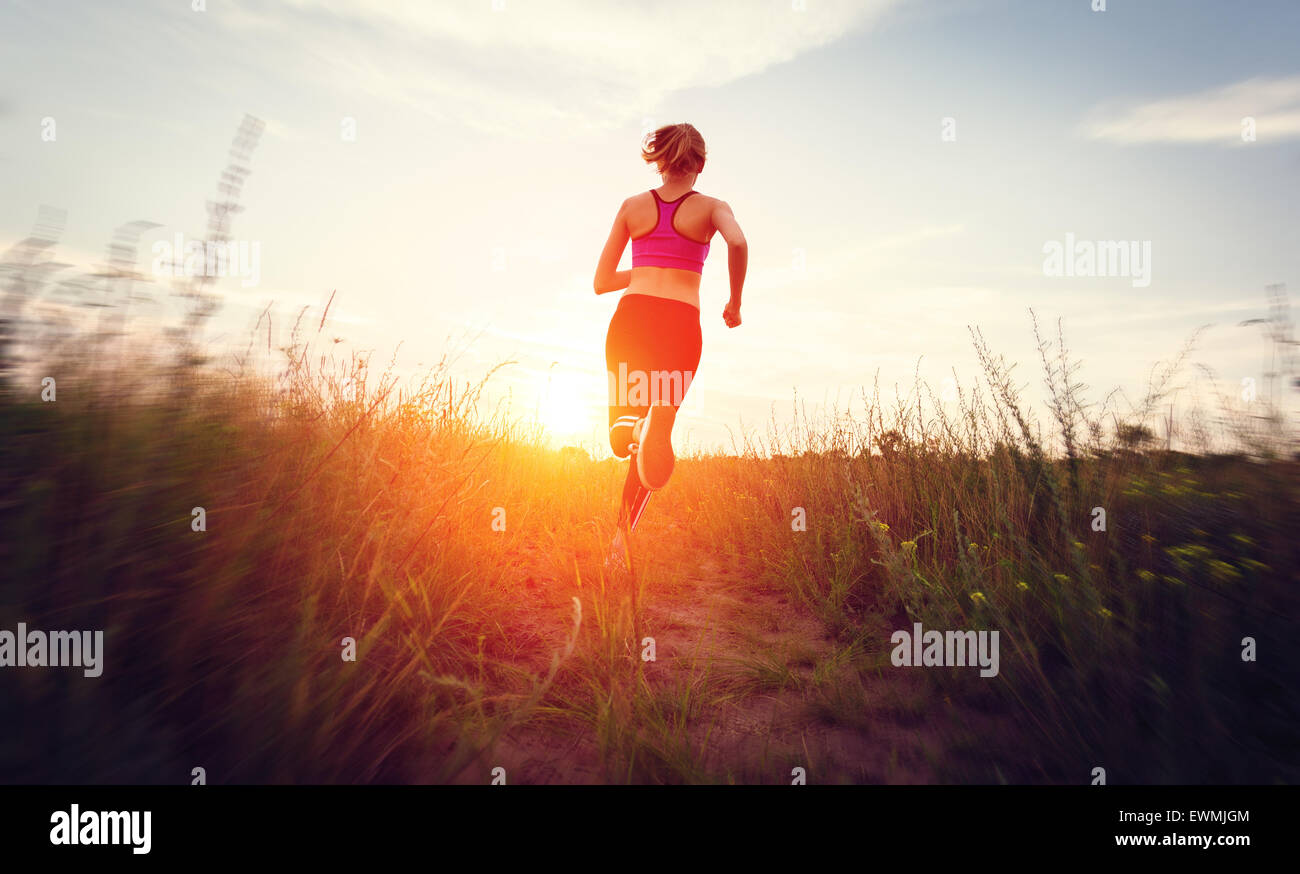 Junge Frau läuft auf einer Landstraße bei Sonnenuntergang in Sommerwiese. Lifestyle-Sport-Hintergrund Stockfoto