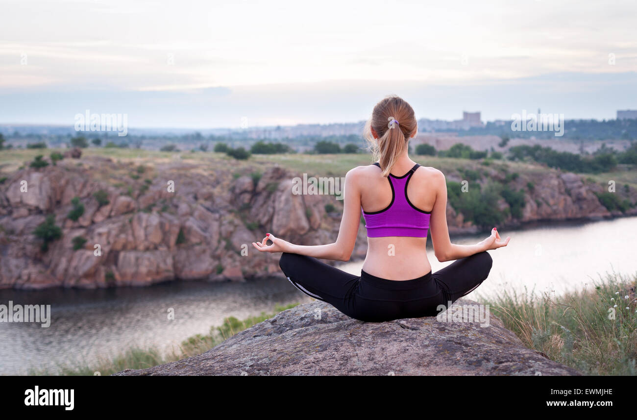 Junge Frau praktizieren Yoga auf dem Hügel bei Sonnenuntergang in der Nähe des Flusses. Stockfoto