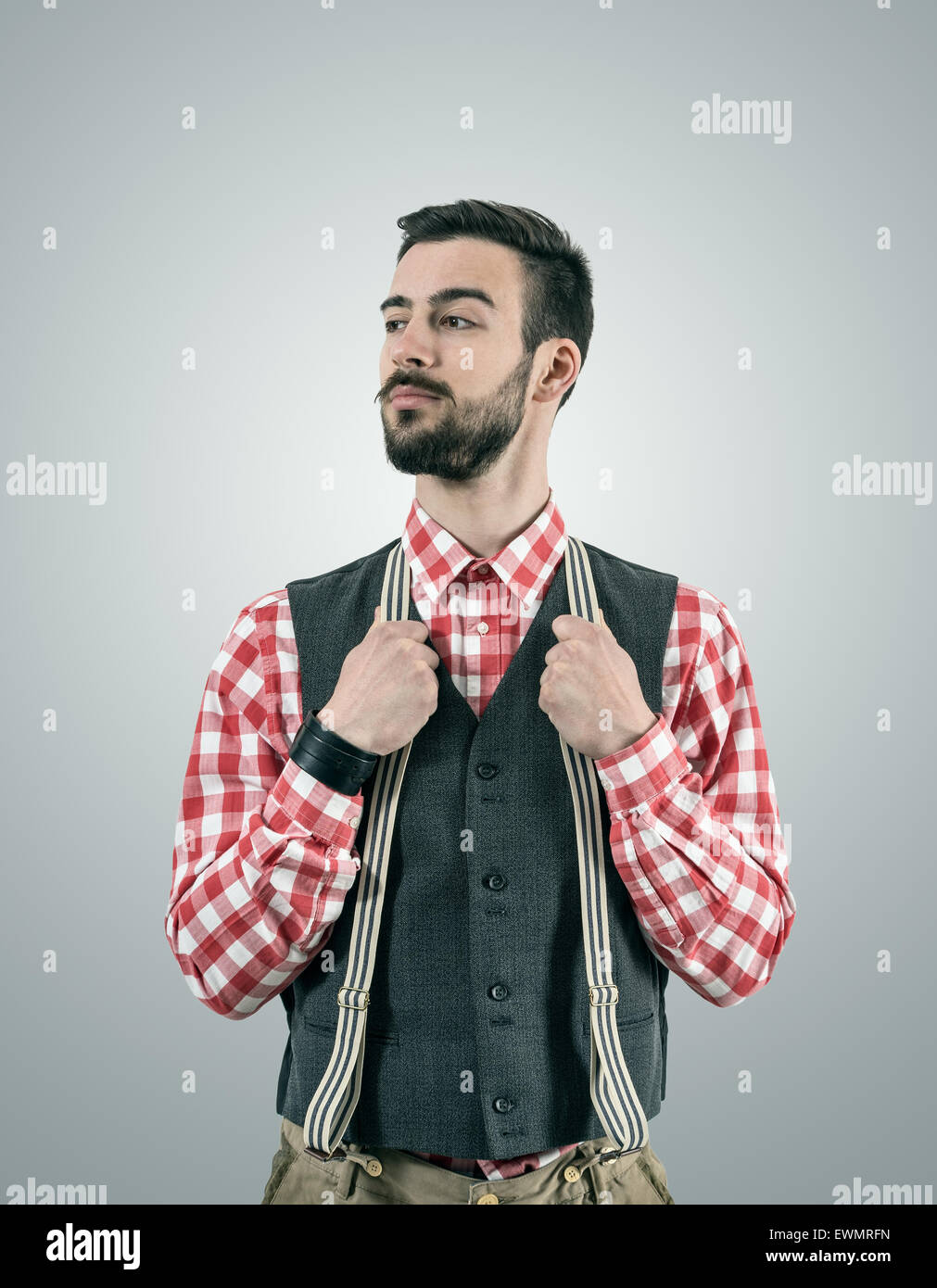 Entsättigt Porträt stehen junge Hipster Modell Wegsehen mit angehobenen Augenbraue halten Sie seine Hosen Hosenträger. Stockfoto