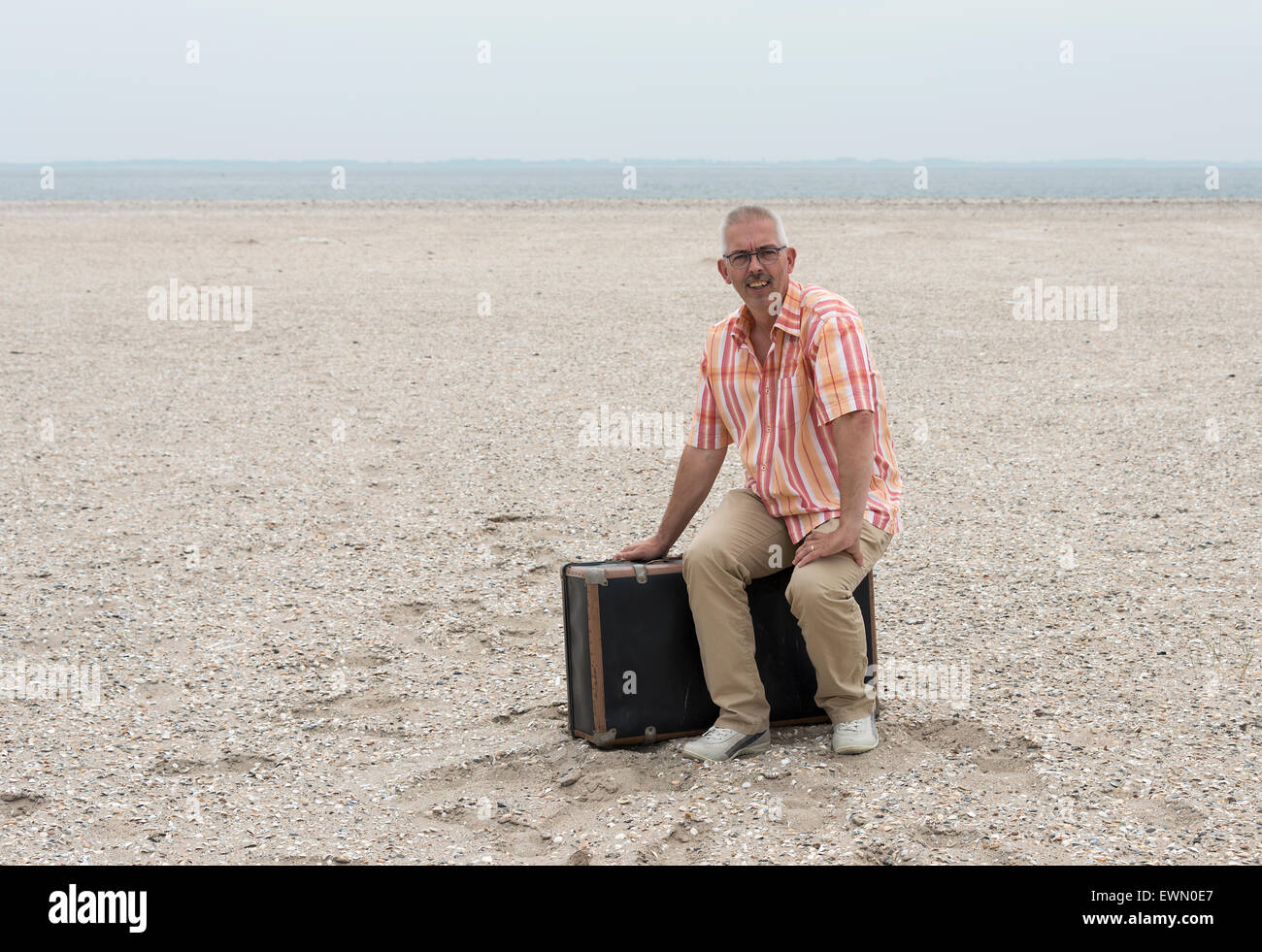 Mann mit alten Koffer am Strand sitzen Reisen Stockfoto