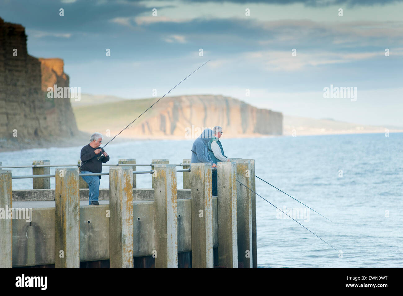 Fischer am Ende von einer Anlegestelle in West Bay, in der Nähe von Bridport in der Grafschaft Dorset, England mit der Jurassic Küste hinter. Stockfoto