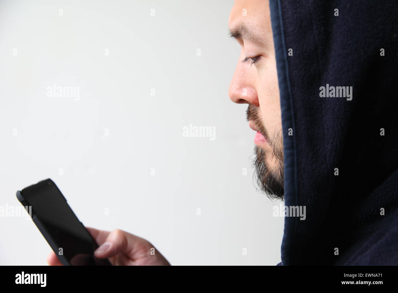 Ein junger Mann trägt eine schwarze Kapuze nutzt sein Handy. Stockfoto