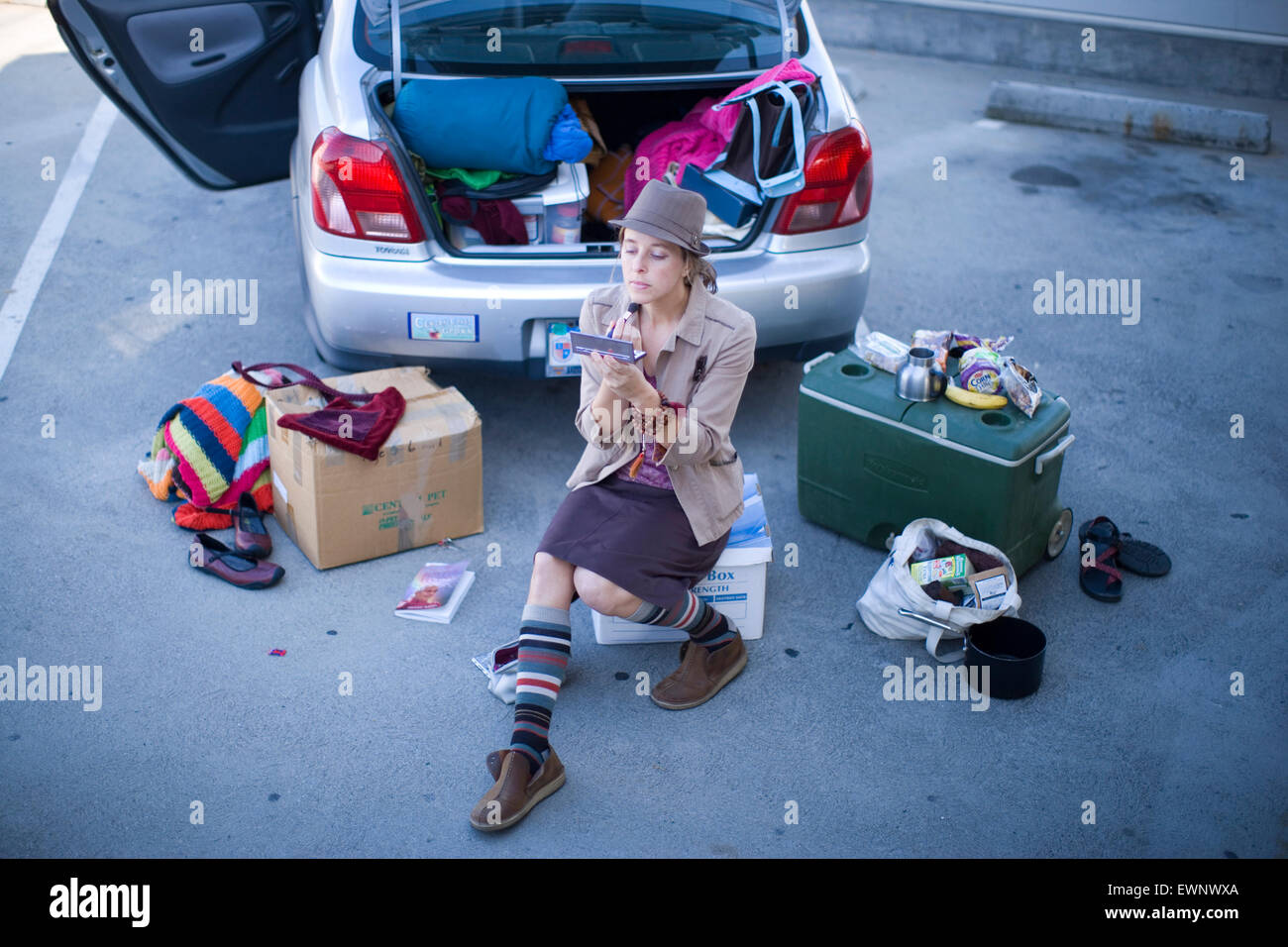 Eine angehende Schauspielerin gilt Make-up vor einem Vorsprechen, sitzend unter ihr Hab und gut in den Kofferraum ihres Autos. Stockfoto