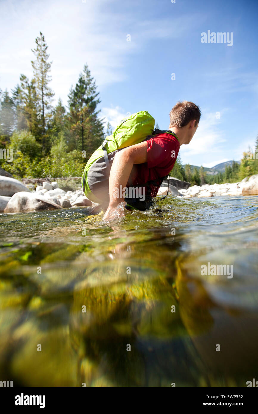 Jungen Erwachsenen Mannes fording einen tiefen Abschnitt eines Flusses tragen ein Tagesrucksack Stockfoto