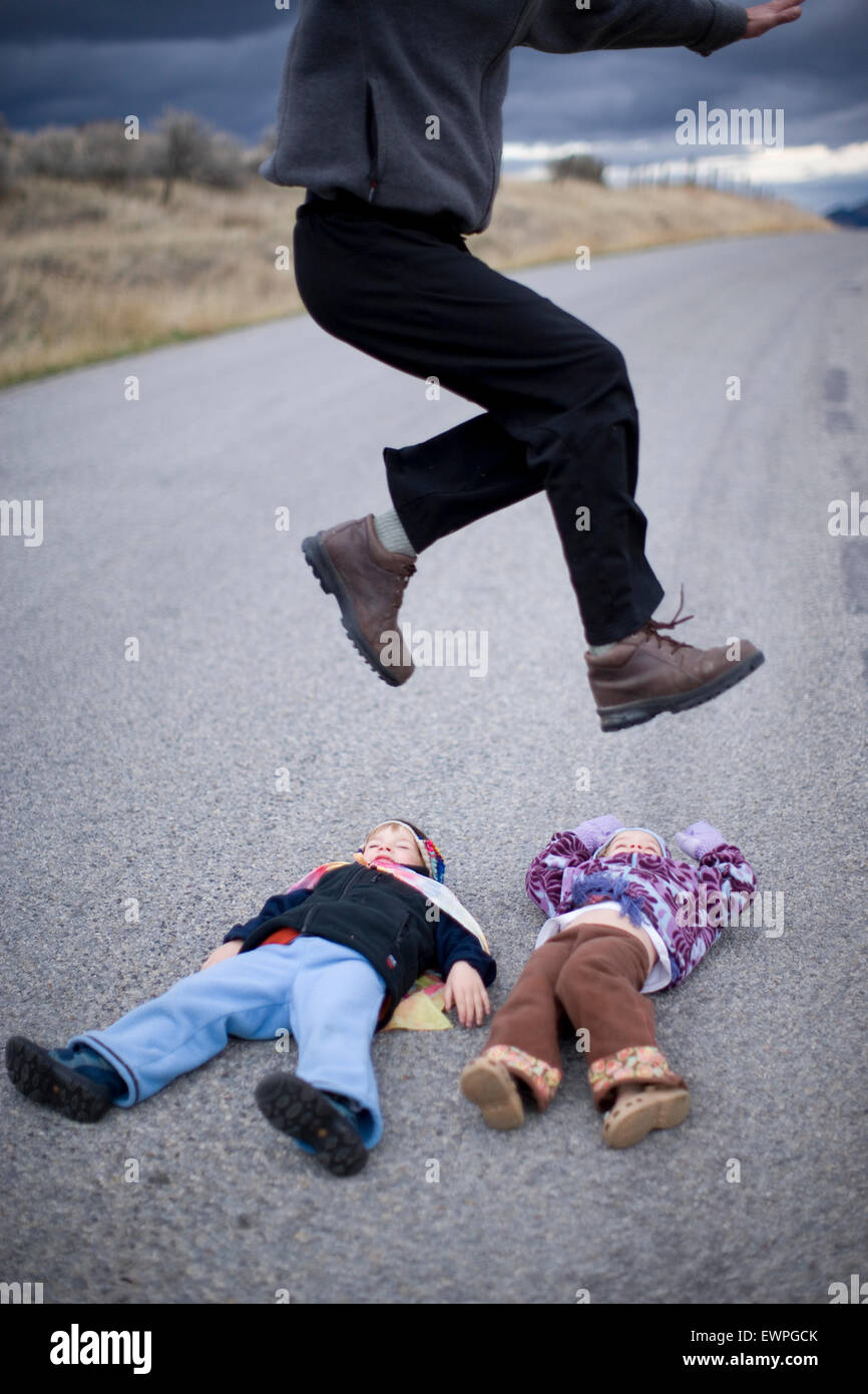 Erwachsener Mann springt über zwei Kinder, die in den Weg legen. Stockfoto